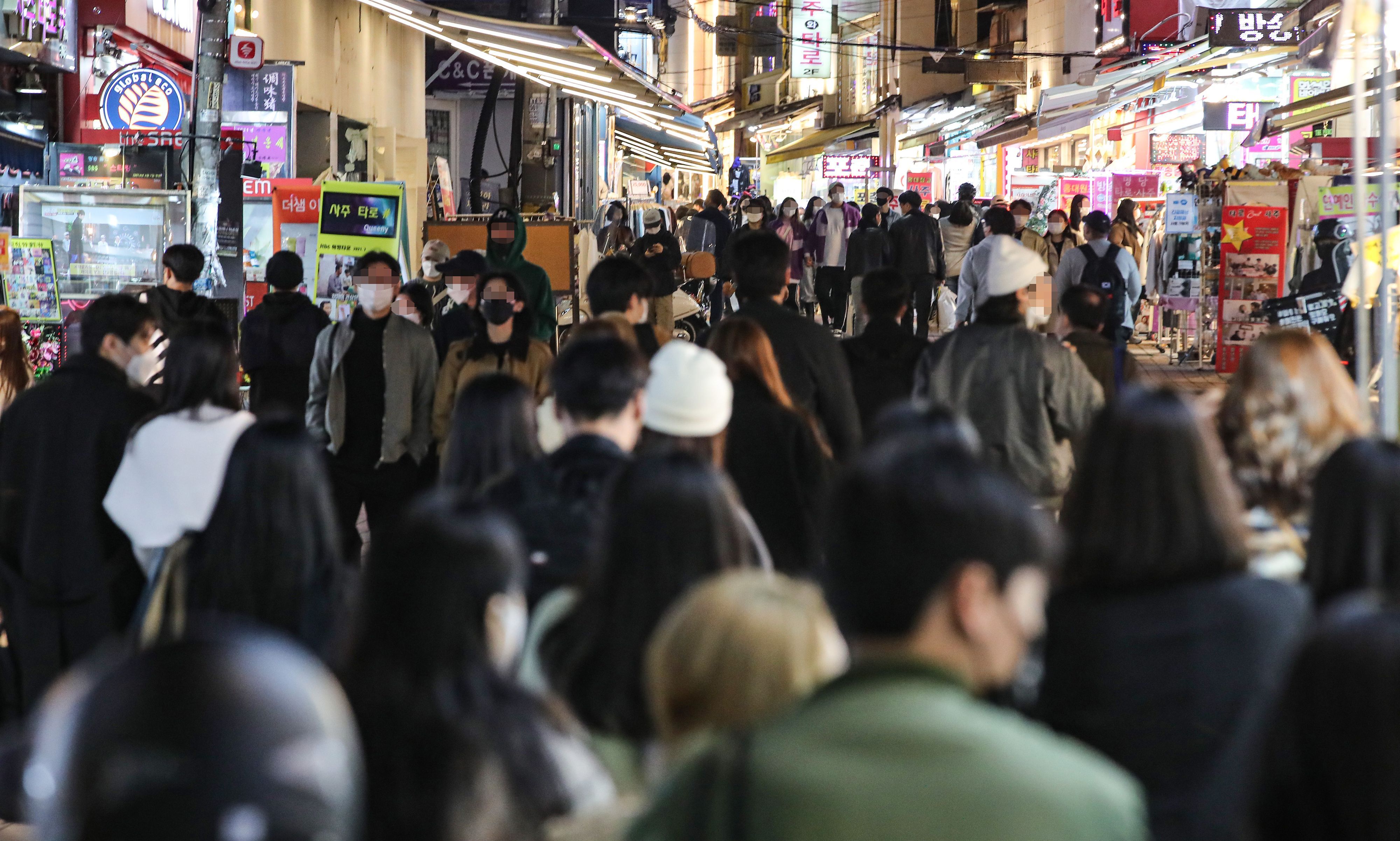 Personen gehen auf einer Straße in einem Vergnügungsviertel in Seoul.
