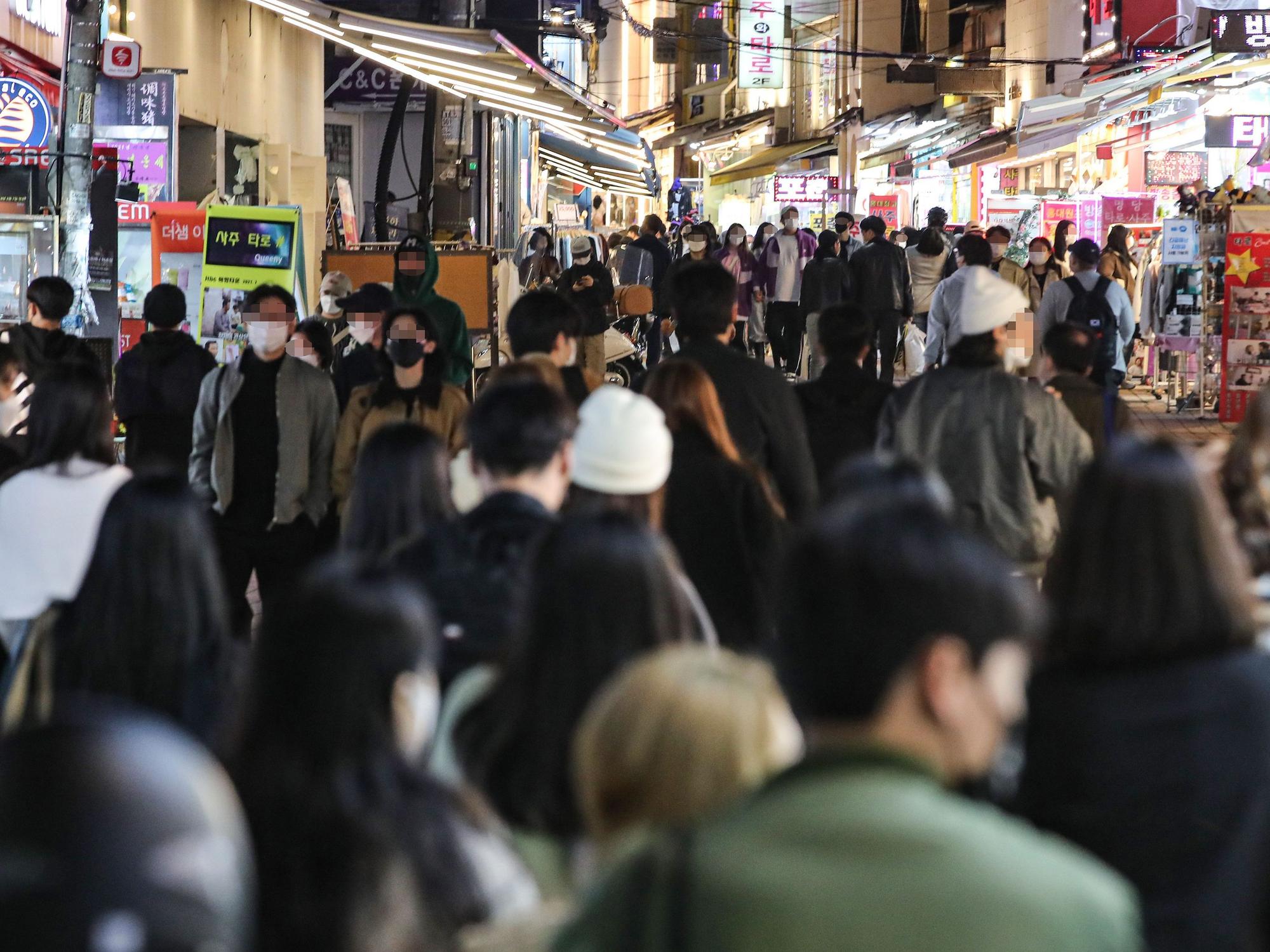 Personen gehen auf einer Straße in einem Vergnügungsviertel in Seoul.