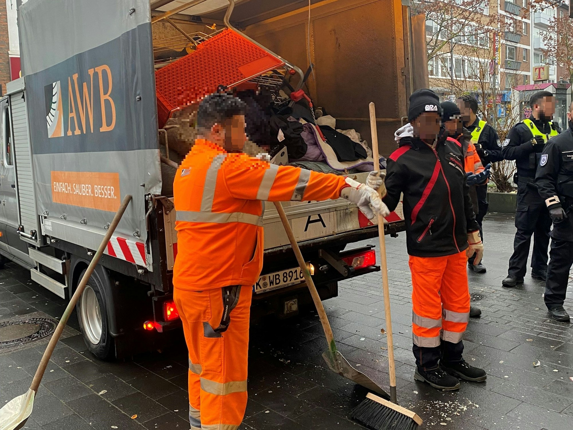 Mitarbeiter von AWB und Ordnungsamt stehen vor einem Müllwagen der AWB und laden Dinge ein.