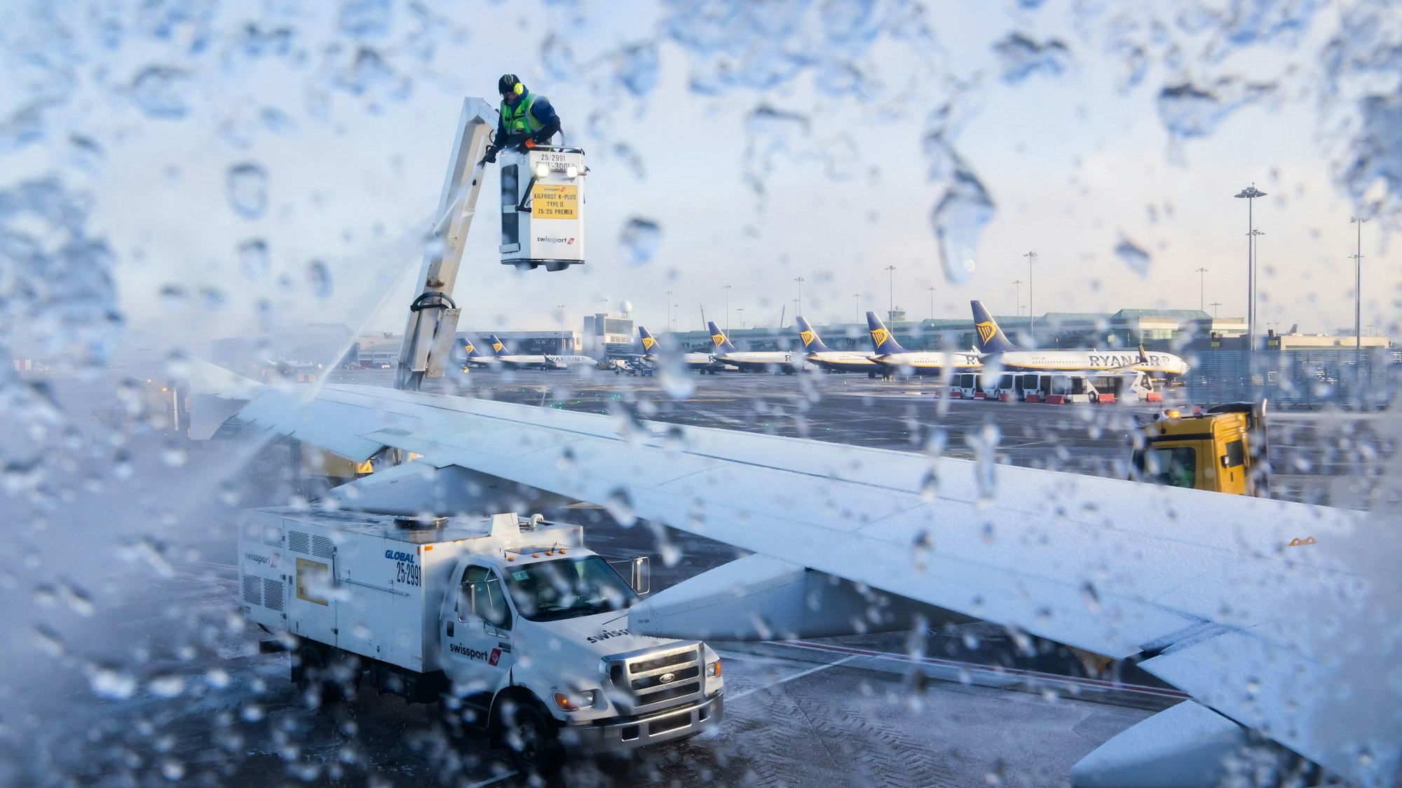 Das Foto zeigt einen Flugzeugflügel, der von einem Mann enteist wird.
