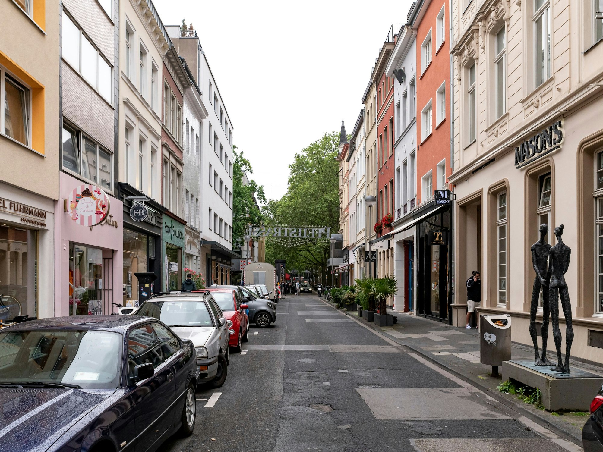 Blick in die Pfeilstraße in Köln. Links und rechts sind Autos geparkt und Fassaden von Geschäften zu sehen.