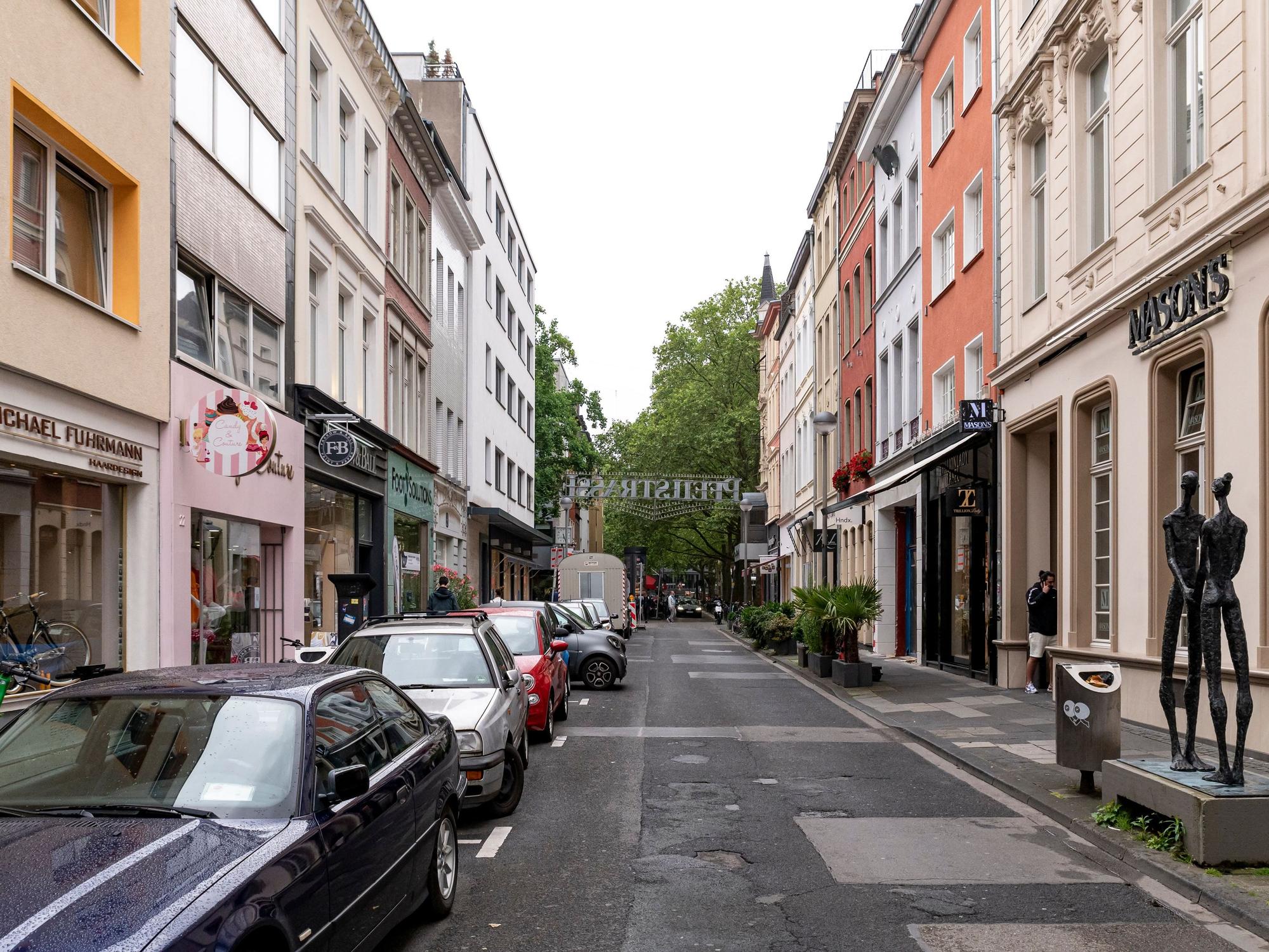 Blick in die Pfeilstraße in Köln. Links und rechts sind Autos geparkt und Fassaden von Geschäften zu sehen.