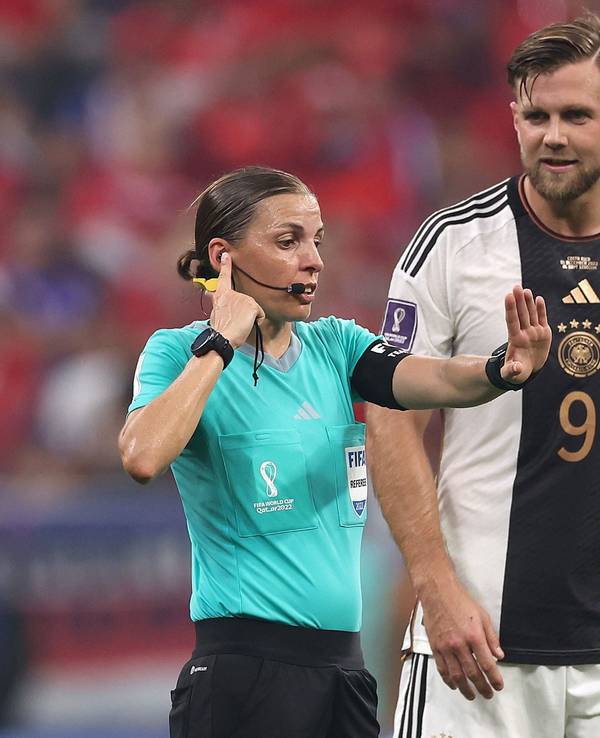 Schiedsrichterin Stéphanie Frappart greift sich bei der WM 2022 mit der Hand ans Ohr und kommuniziert mit dem VAR. Deutschland-Stürmer Niclas Füllkrug schaut interessiert.