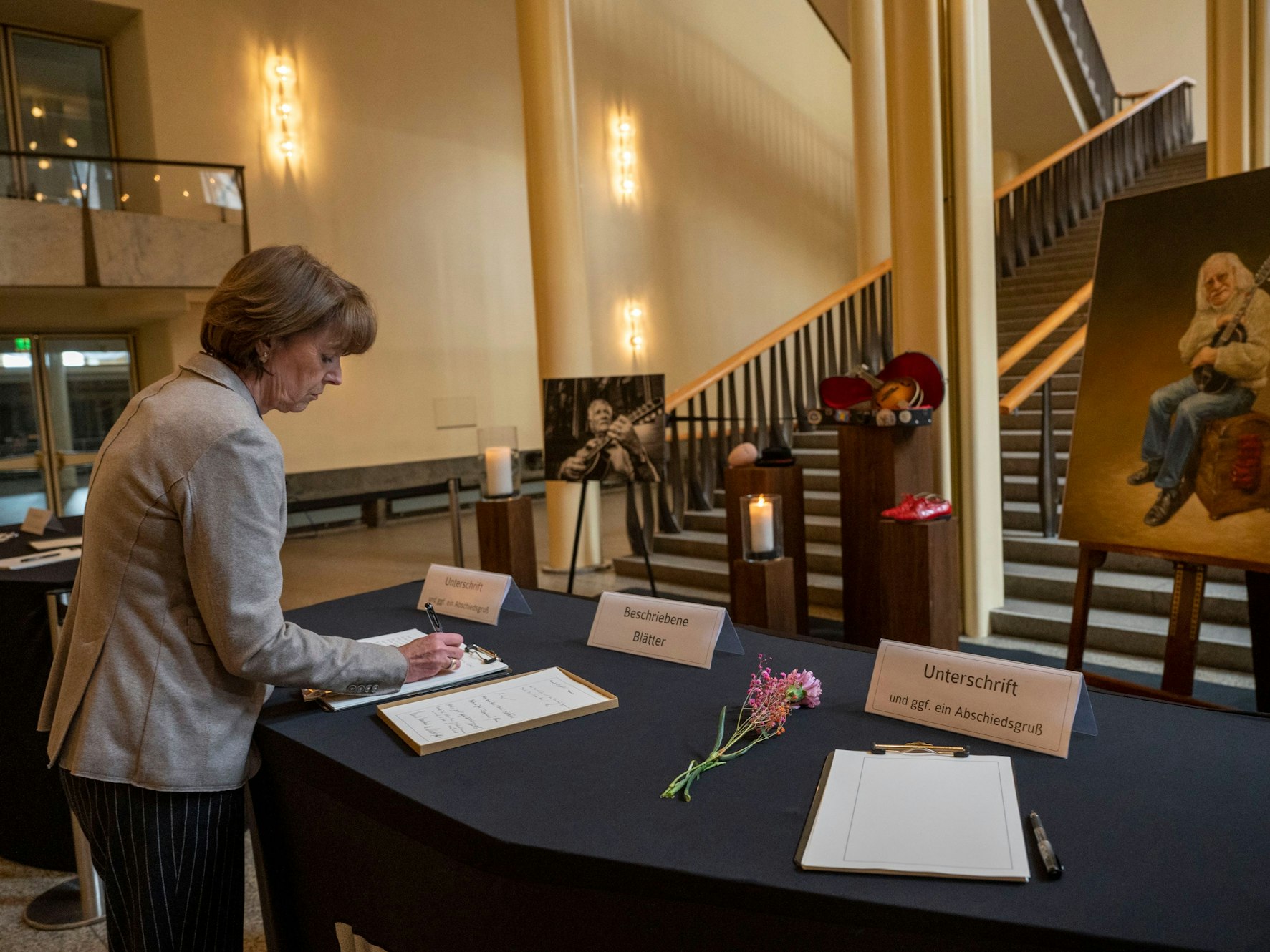 Kölns OB Henriette Reker steht vor einem Bild von Hans Süper und schreibt Zeilen in das Kondolenzbuch.