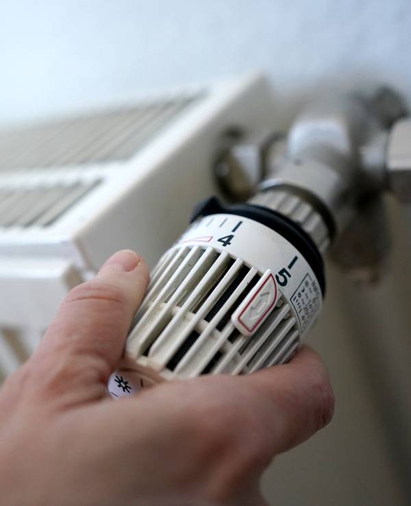 Eine Frau dreht an einem Heizungsthermostat.