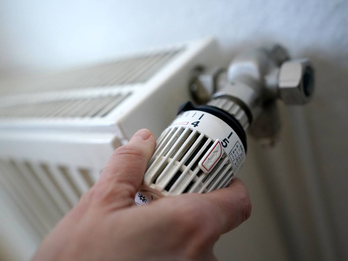Eine Frau dreht an einem Heizungsthermostat.