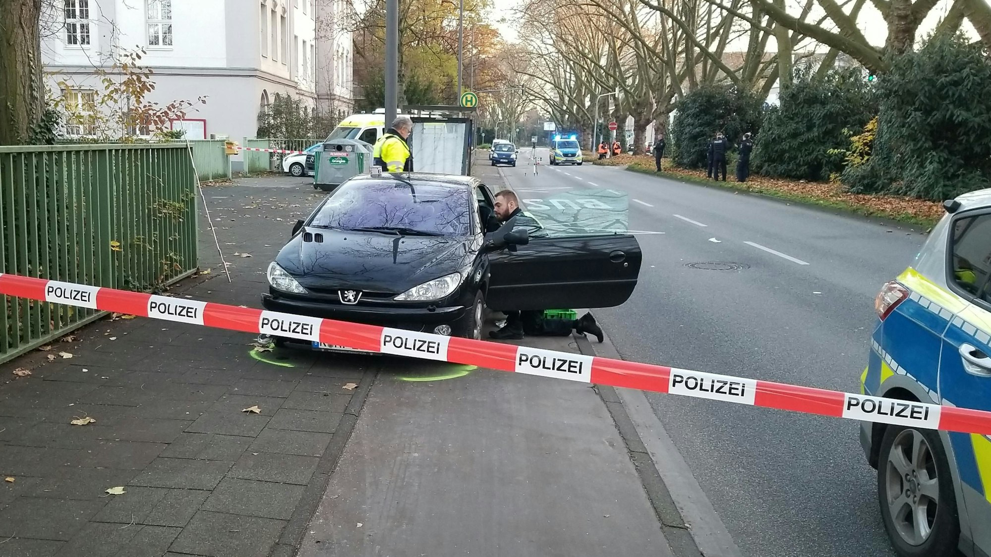Die Polizei hat einen Gehweg abgesperrt. Hinter dem Flatterband steht ein Auto, vor der geöffneten Fahrertür kniet ein Polizist.