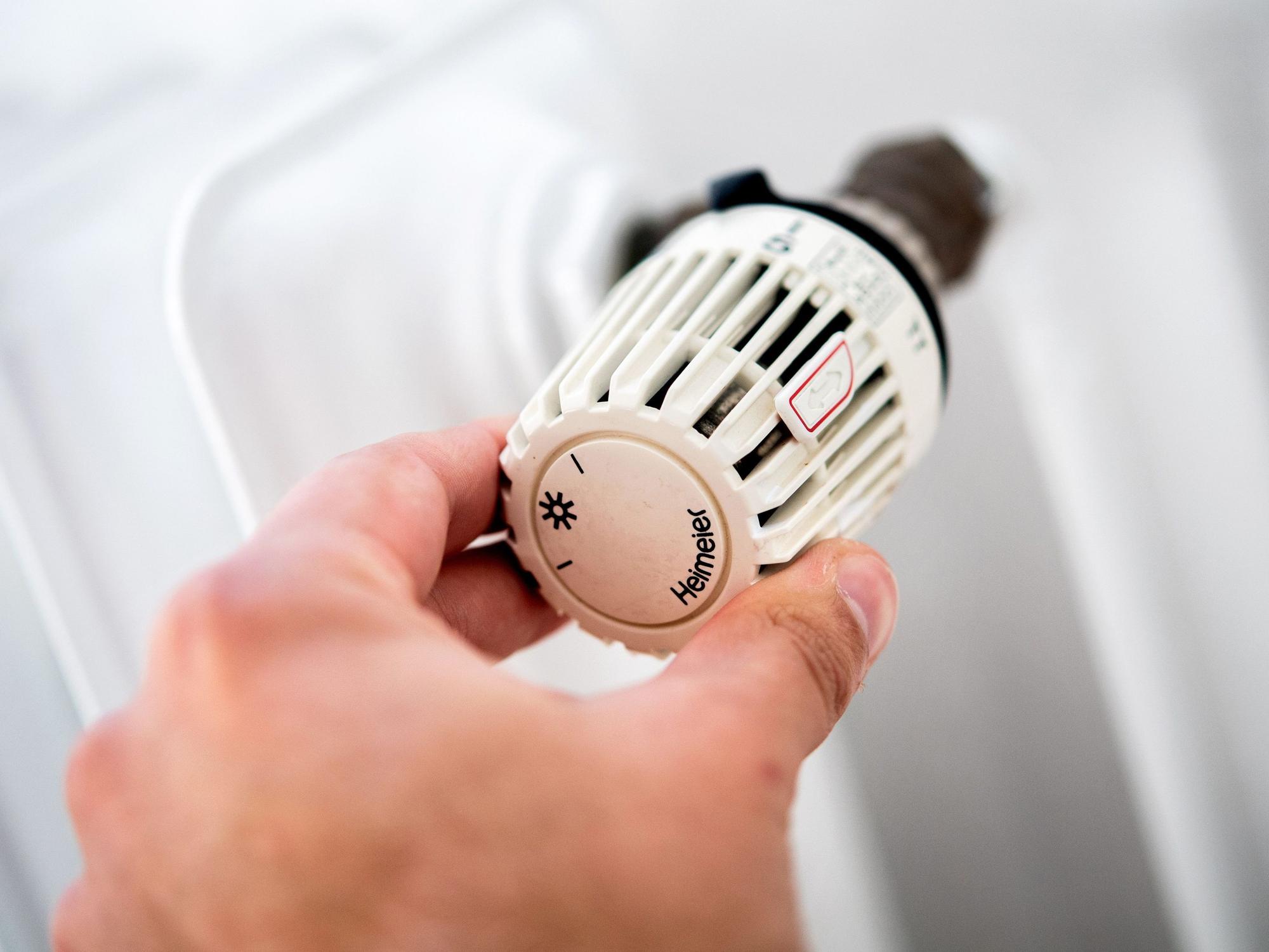 Ein Mann dreht in einer Wohnung am Thermostat einer Heizung.