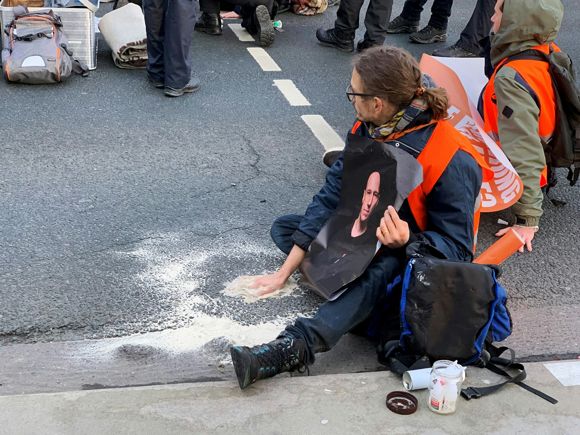 Ein Aktivist der Gruppe „Letzte Generation“ sitzt mit einer auf dem Asphalt festgeklebten Hand auf einer mehrspurigen Straße am Hauptbahnhof in Mainz.