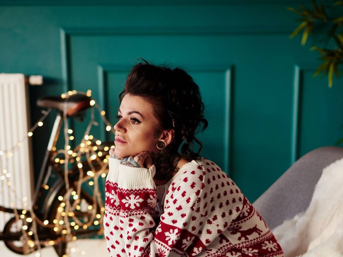 Junge Frau sitzt traurig im Weihnachtspullover vor einer Lichterkette.