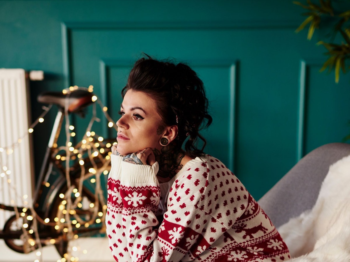 Junge Frau sitzt traurig im Weihnachtspullover vor einer Lichterkette.