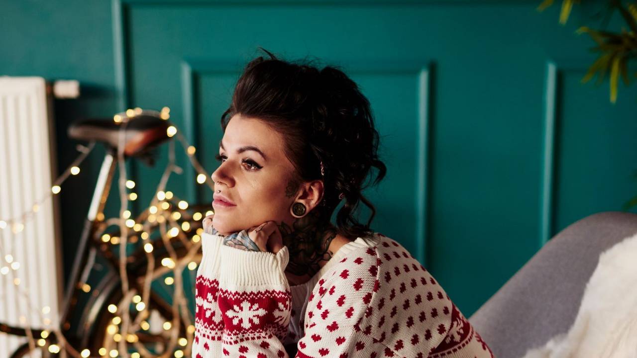 Junge Frau sitzt traurig im Weihnachtspullover vor einer Lichterkette.