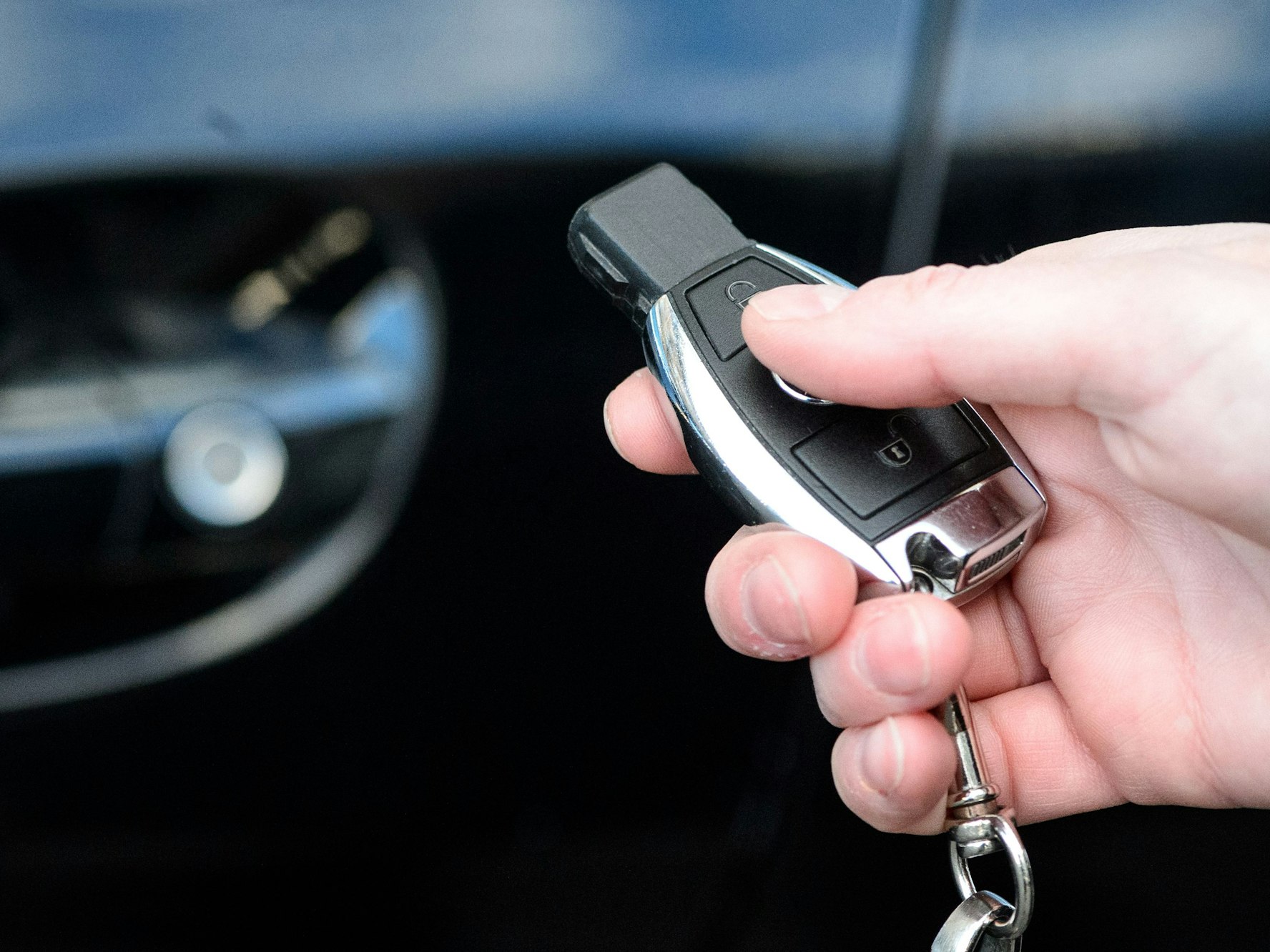 Eine Person hält einen Autoschlüssel in der Hand. Im Hintergrund ist das Fahrzeug zu sehen.