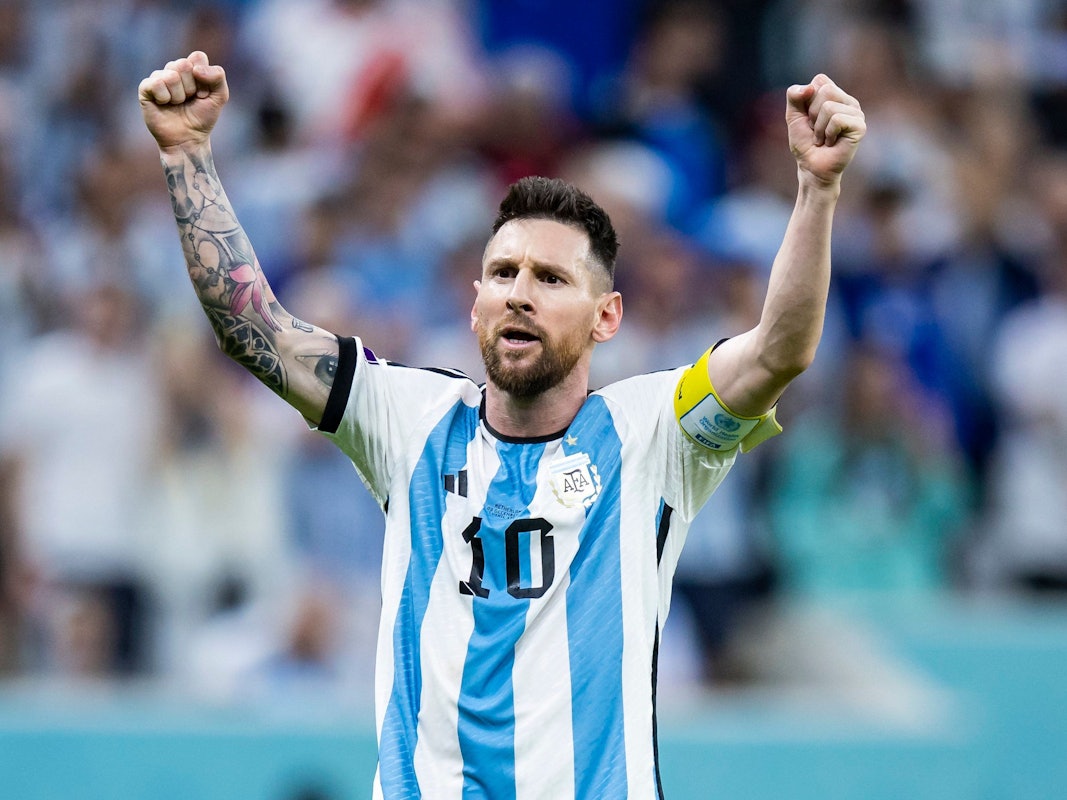 Lionel Messi steht im Trikot von Argentinien mit der Nr. 10 vor der Kurve und reckt beide Fäuste in die Höhe.