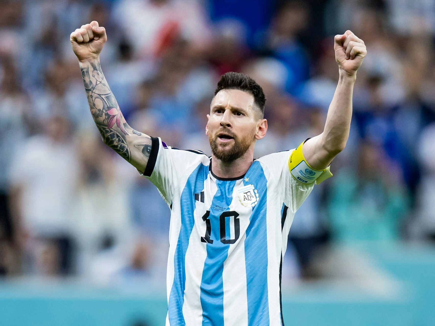 Lionel Messi steht im Trikot von Argentinien mit der Nr. 10 vor der Kurve und reckt beide Fäuste in die Höhe.