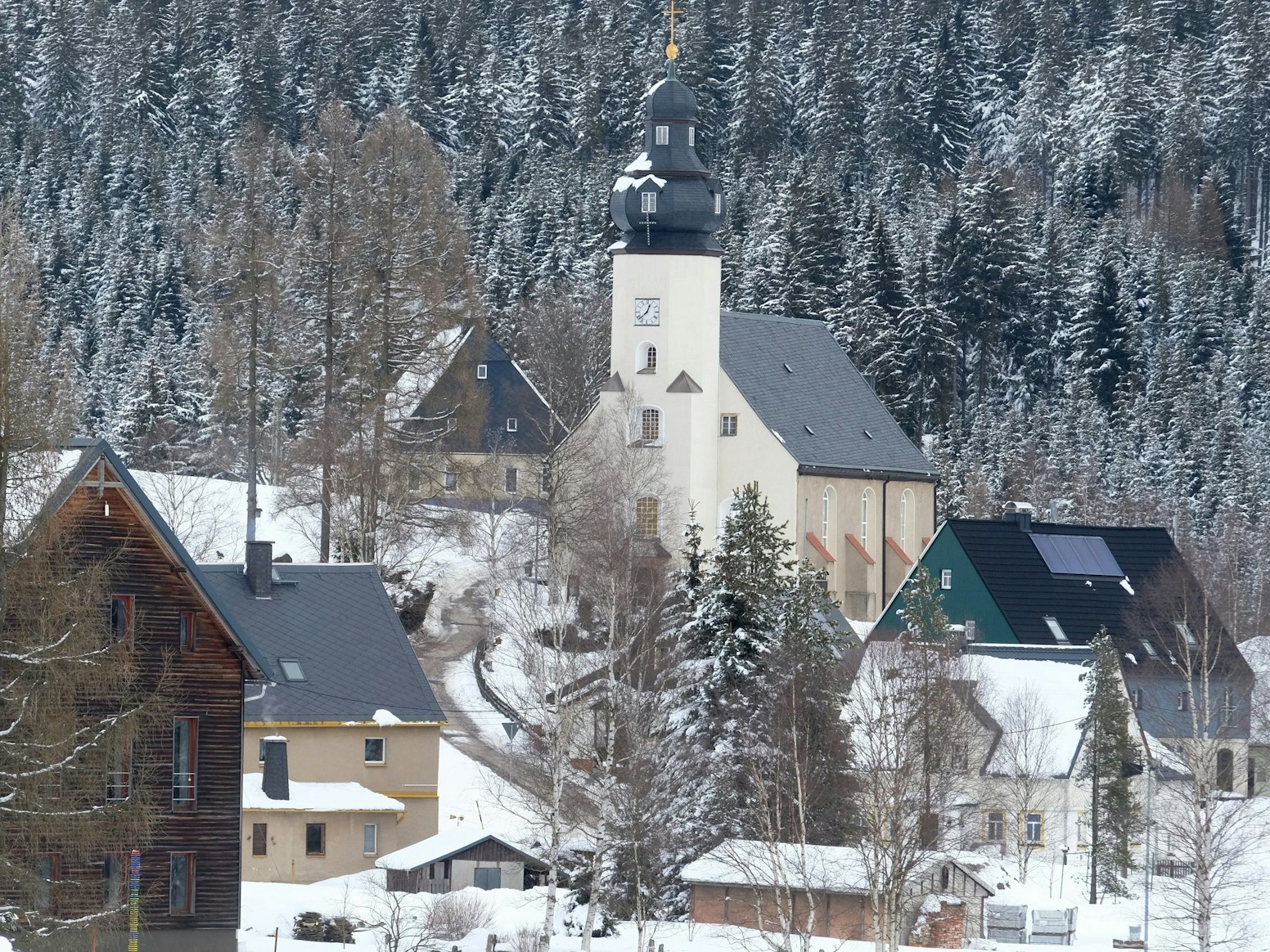 Die Kirche und Häuser von Kühnhaide, einem Ortsteil der sächsischen Stadt Marienberg im Erzgebirgskreis, sind von Schnee umgeben.