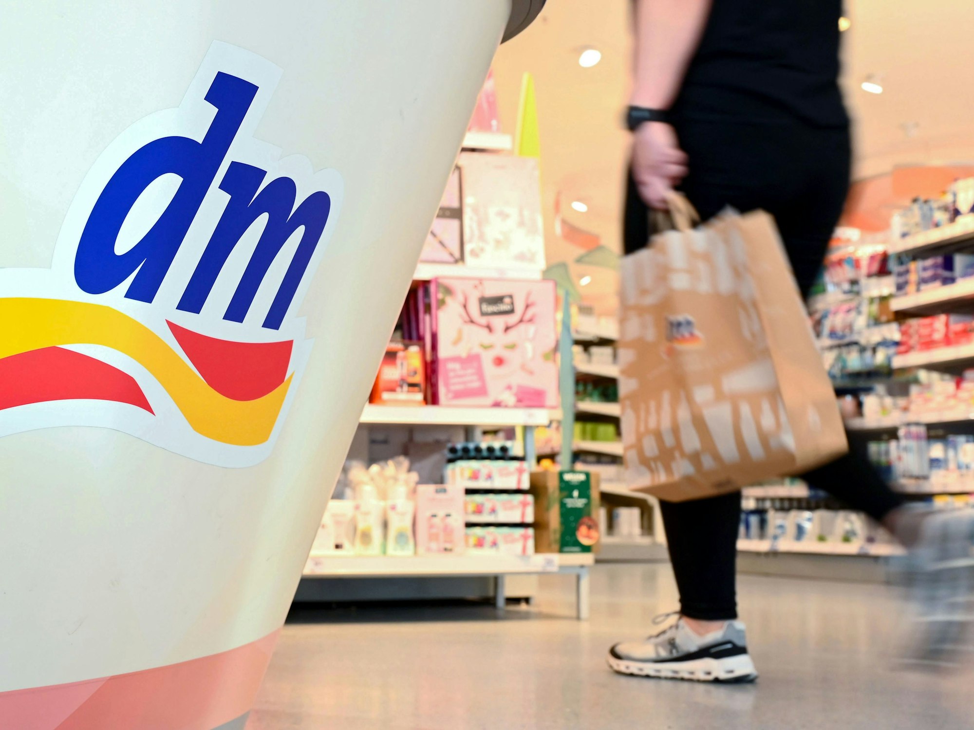 Eine Person geht in einer Filiale der Drogeriemarktkette dm mit einer Einkaufstüte am Kassenbereich vorbei.