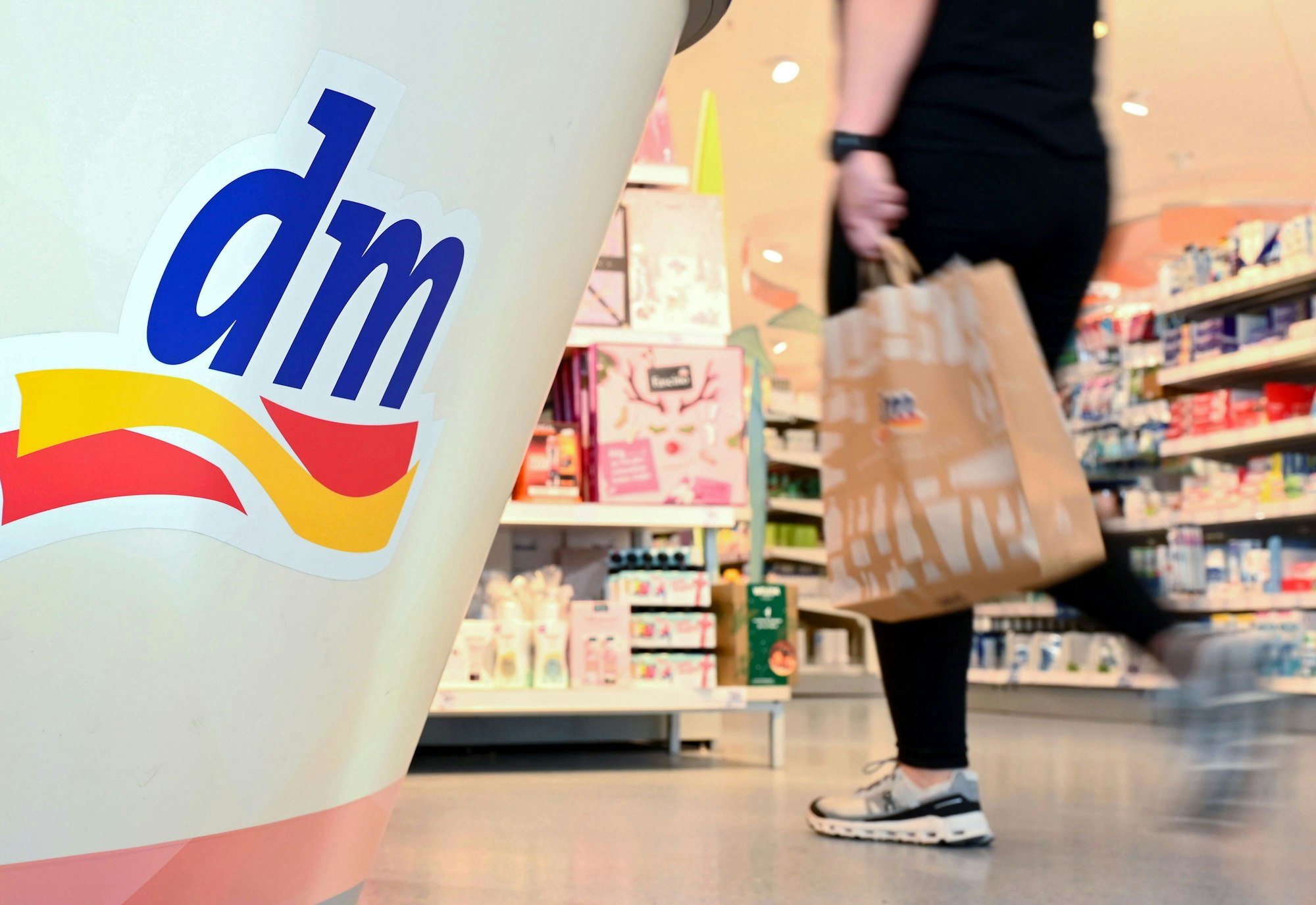 Eine Person geht in einer Filiale der Drogeriemarktkette dm mit einer Einkaufstüte am Kassenbereich vorbei.