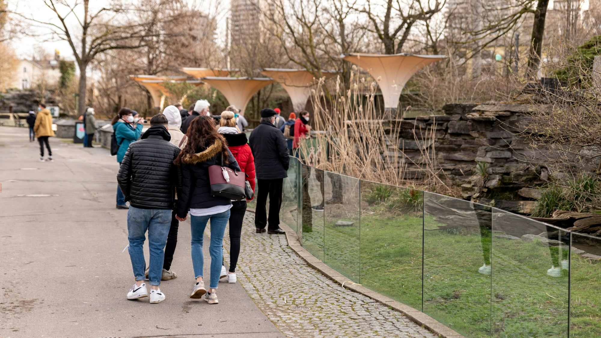 Menschen gehen in dicken Klamotten durch den Kölner Zoo. Rechts ist ein kleineres Gehege zu sehen.