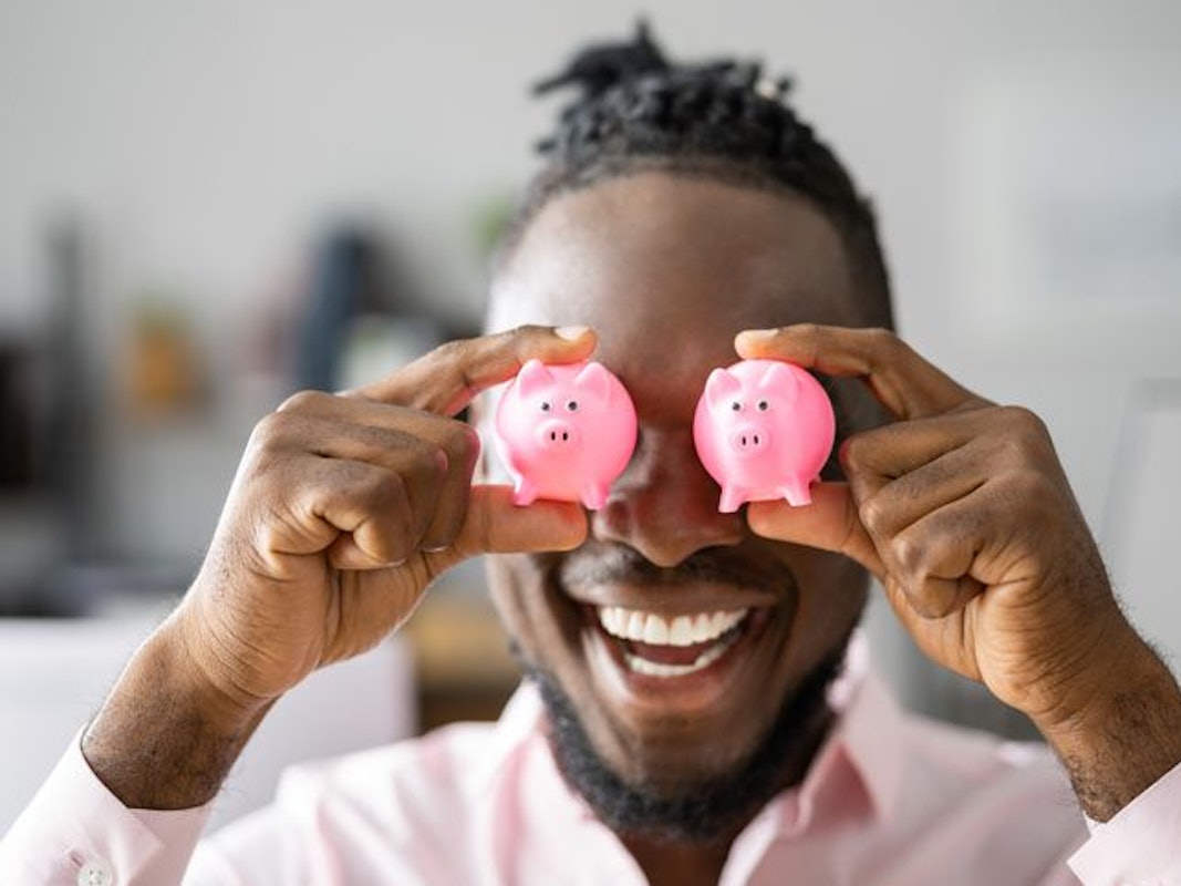 Mann hält sich zwei rosa mini-Sparschweinchen vor die Augen.