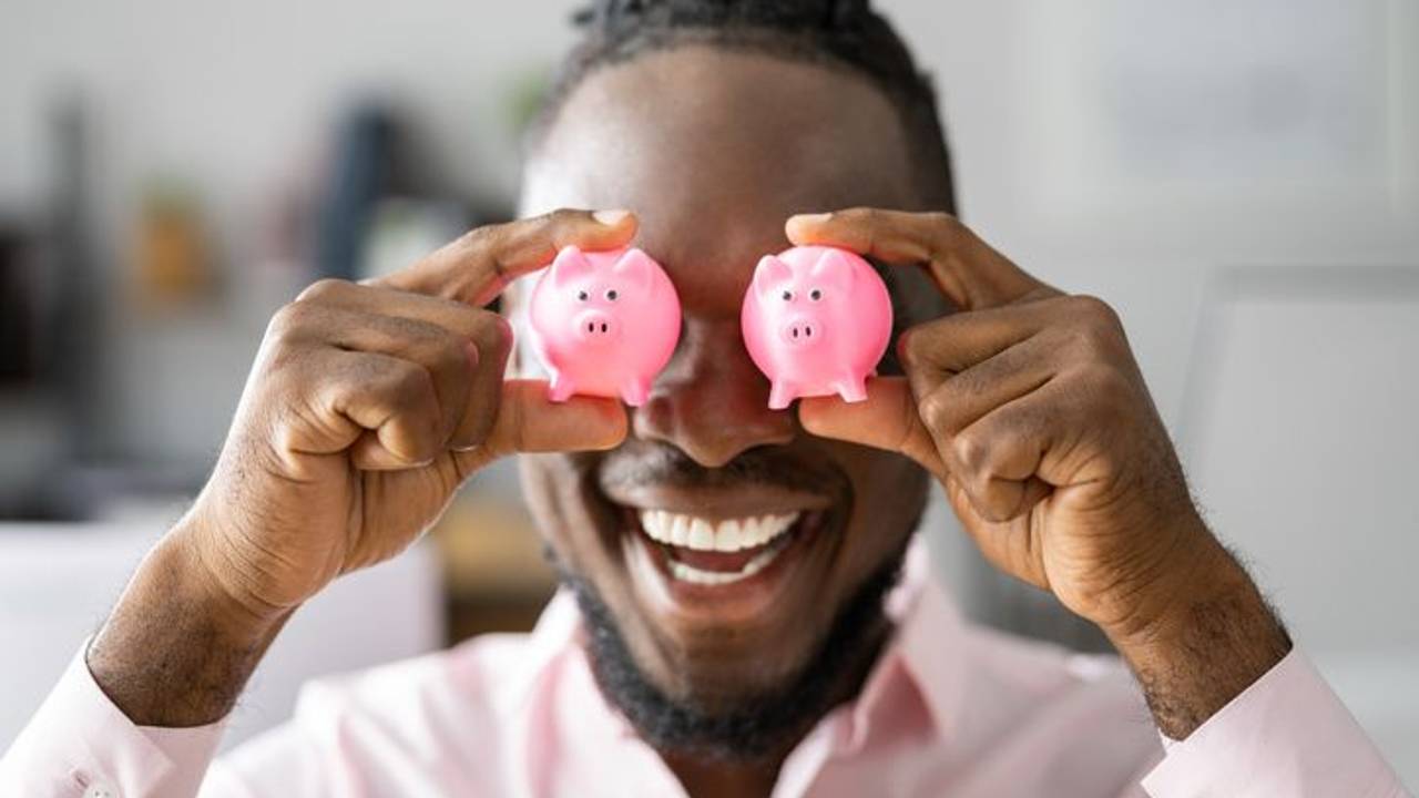 Mann hält sich zwei rosa mini-Sparschweinchen vor die Augen.