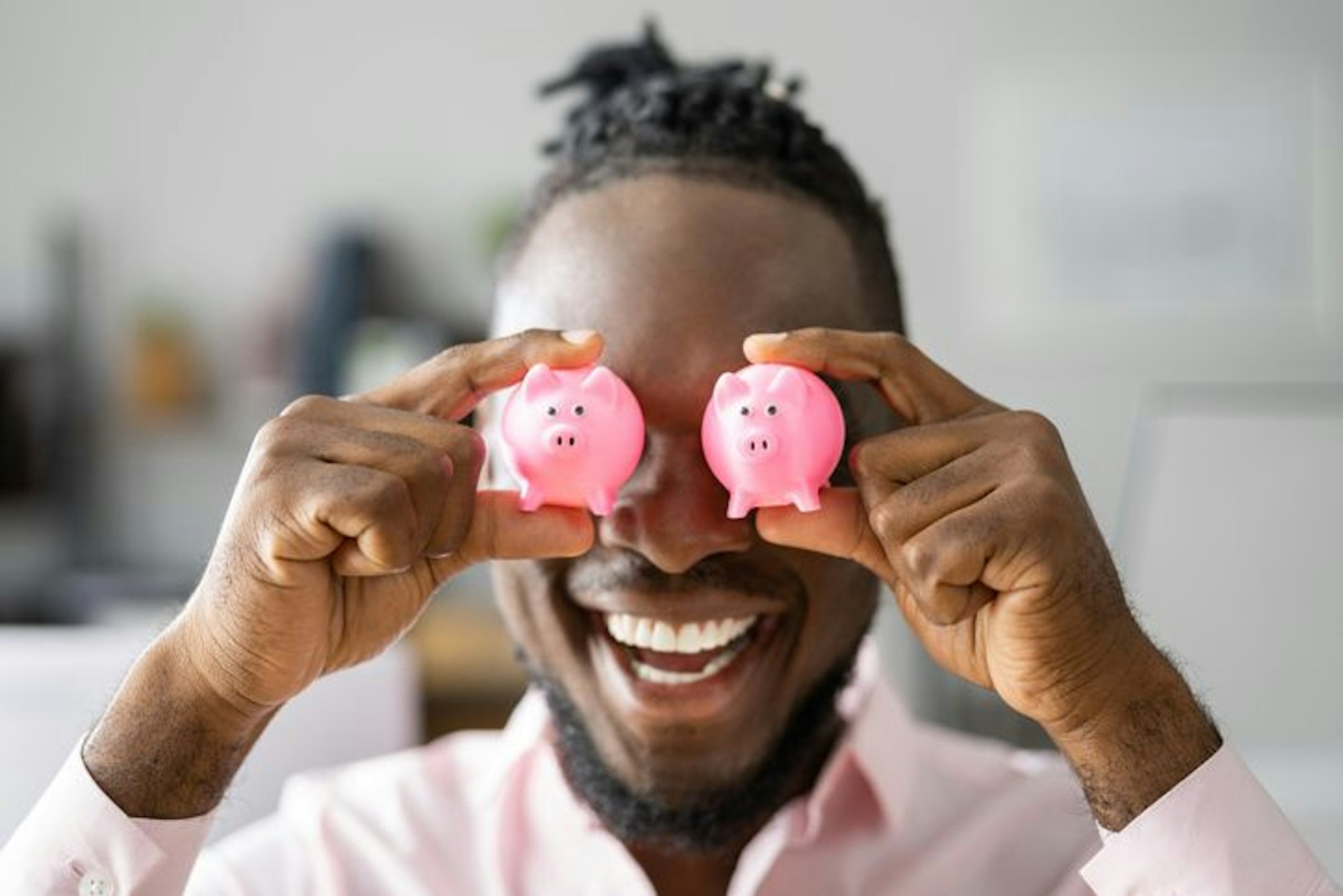 Mann hält sich zwei rosa mini-Sparschweinchen vor die Augen.