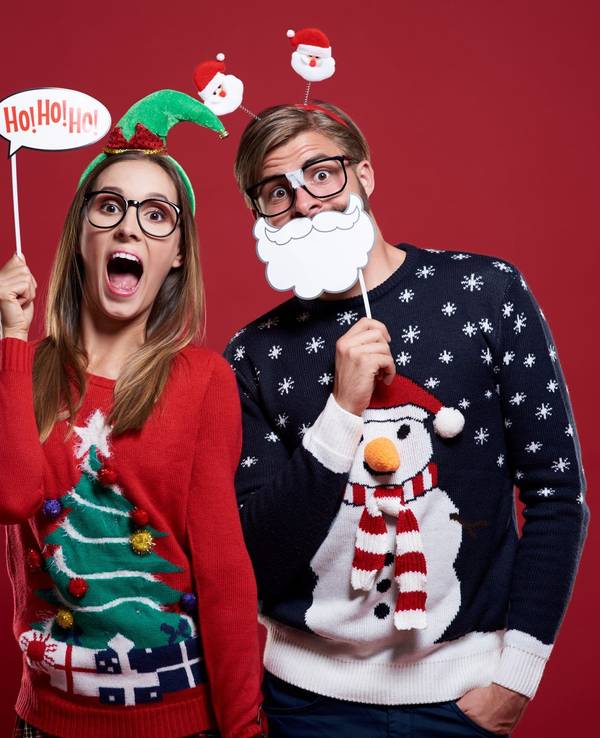 Ein Pärchen in Weihnachtspullovern mit Deko-Artikeln.