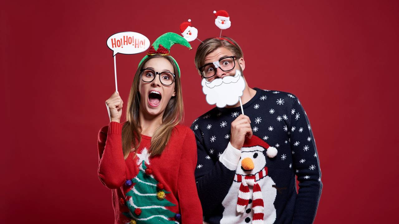 Ein Pärchen in Weihnachtspullovern mit Deko-Artikeln.