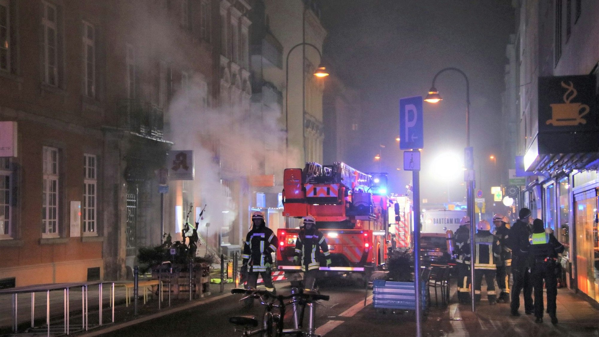 Aus der Apotheke dringt Qualm, davor stehen ein Löschfahrzeug sowie zahlreiche Feuerwehrleute im Bereich der Straße.