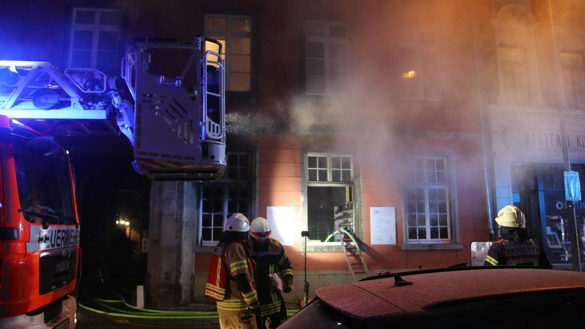 Einsatzkräfte der Feuerwehr stehen vor einem Haus, in dessen Parterre sich eine Apotheke befindet.