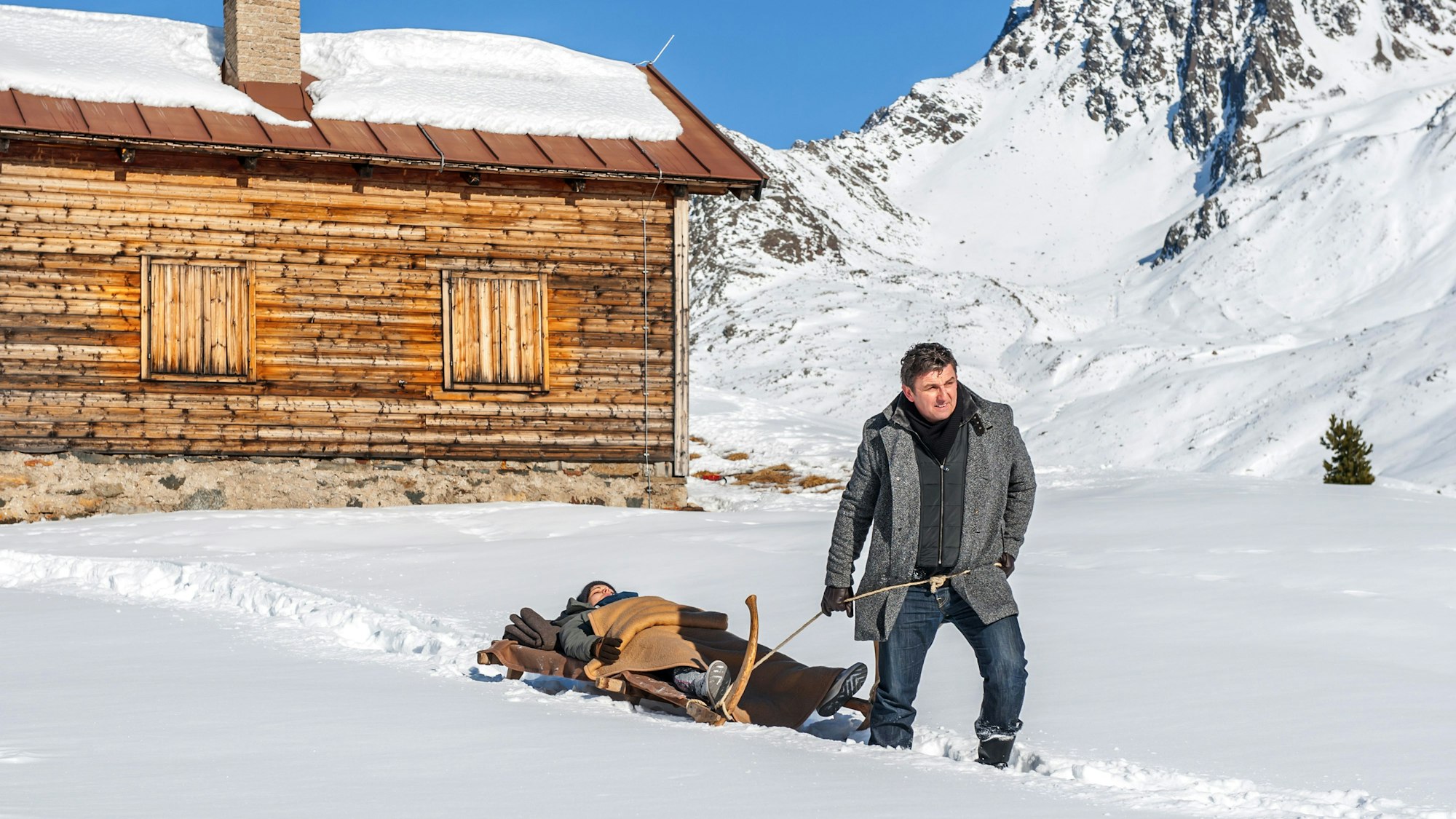Hans Sigl als Martin Gruber zieht Henriette Richter-Röhl als Lisa auf einem Schlitten in einer Szene aus der Fernsehserie „Der Bergdoktor“.