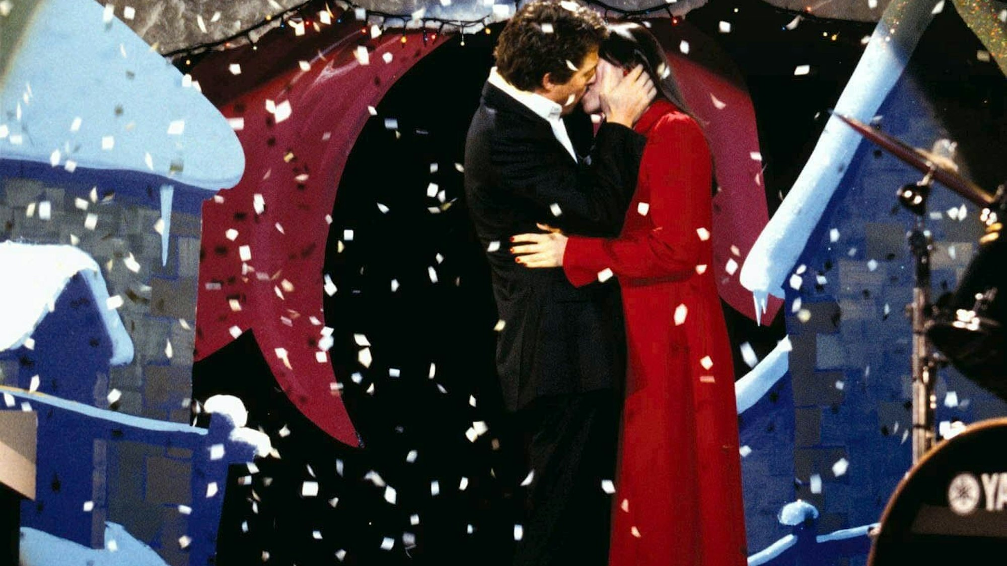 Der englische Premierminister (gespielt von Hugh Grant) küsst seine Angestellte Natalie (gespielt von Martine McCutcheon) auf einer Bühne. Von oben rieselt weißes Konfetti auf die beiden herab.