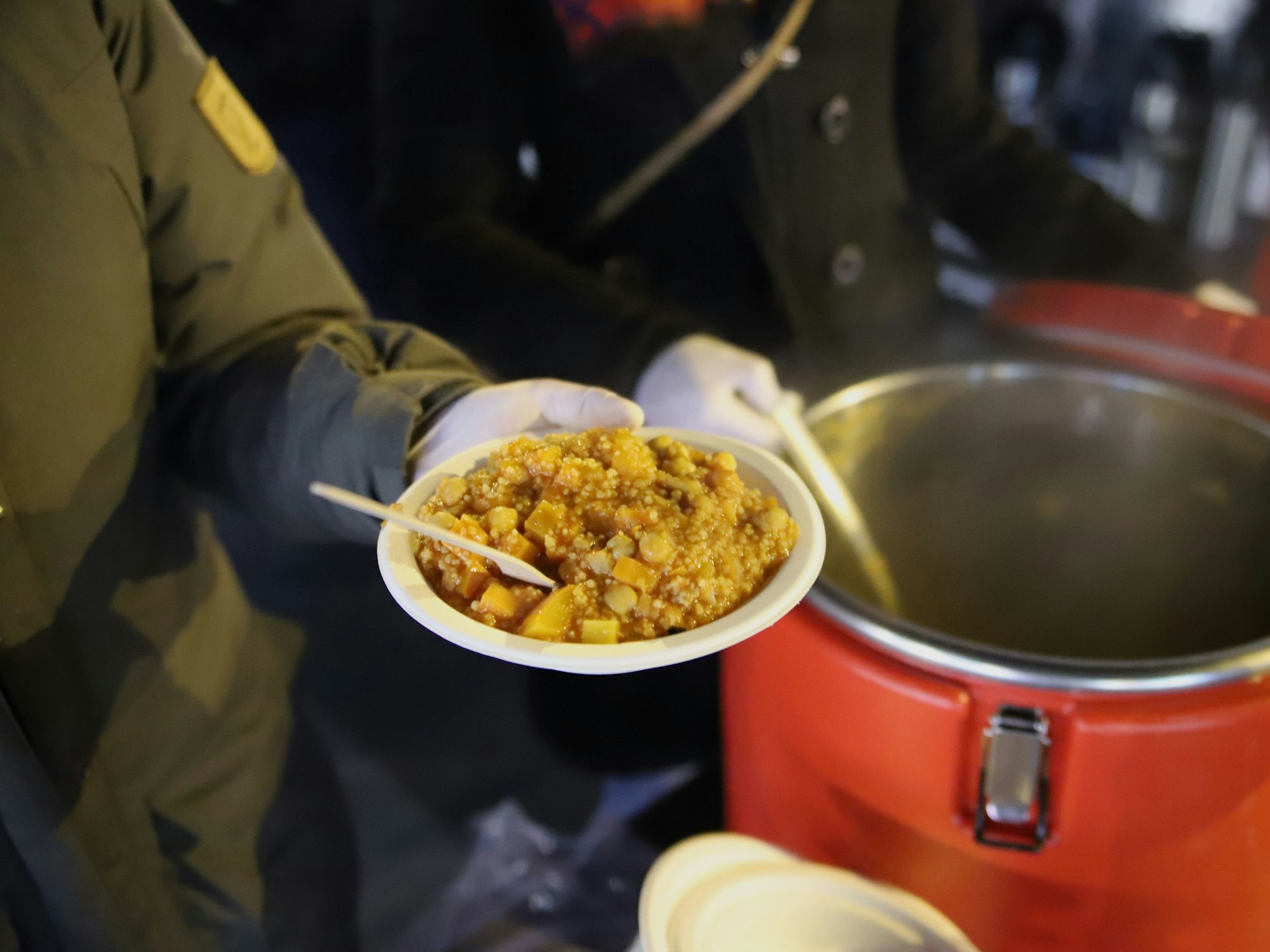Eine Frau hält einen Teller mit Eintopf in der Hand.