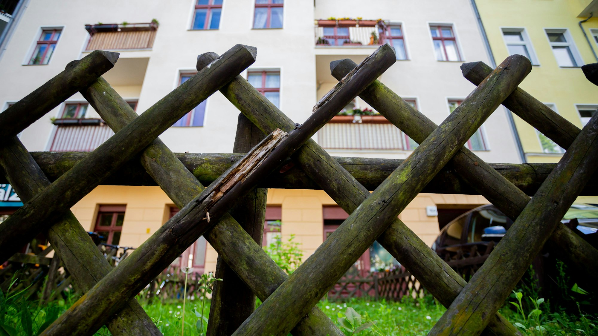 Ein Jägerzaun steht vor einem gelben Wohnhaus.