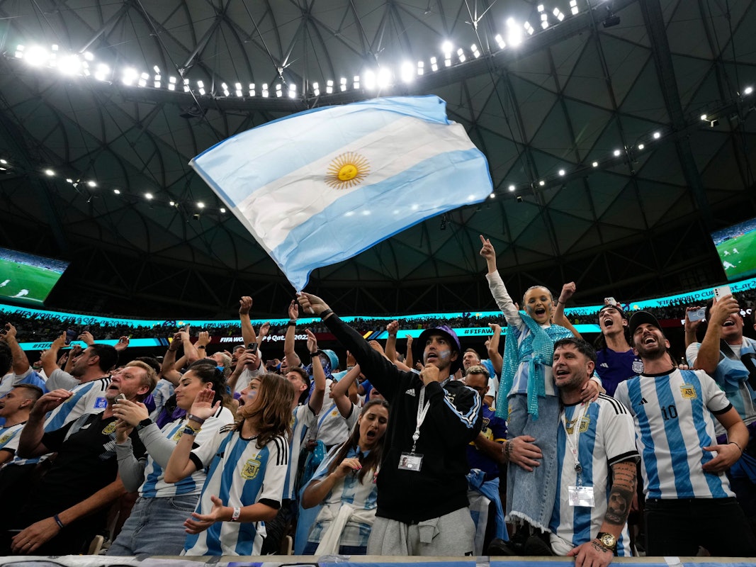 Argentinien-Fans singen bei einem WM-Spiel lautstark und schwenken eine argentinische Flagge.