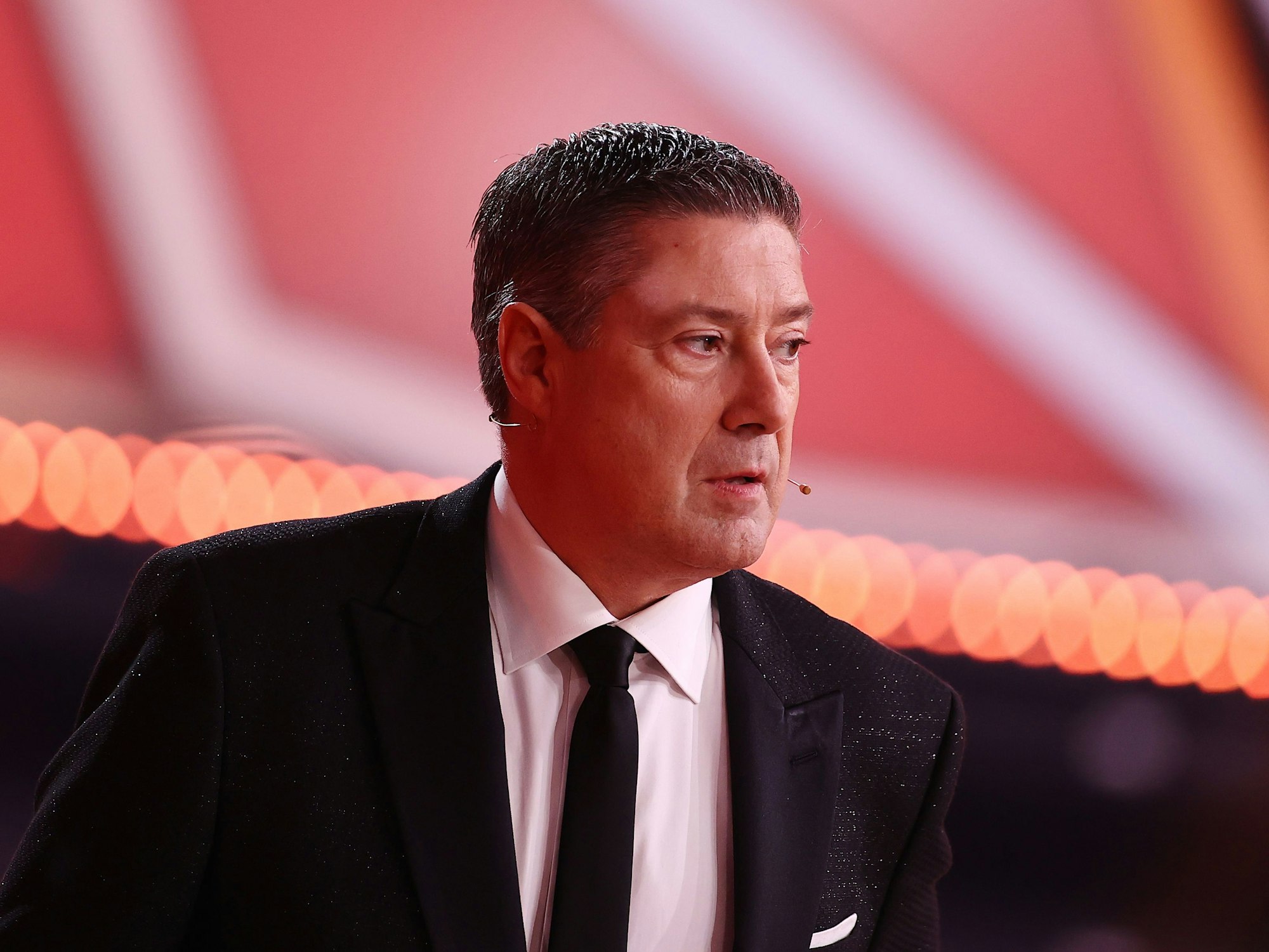 Joachim Llambi steht im Anzug auf der Bühne und schaut zur Seite.