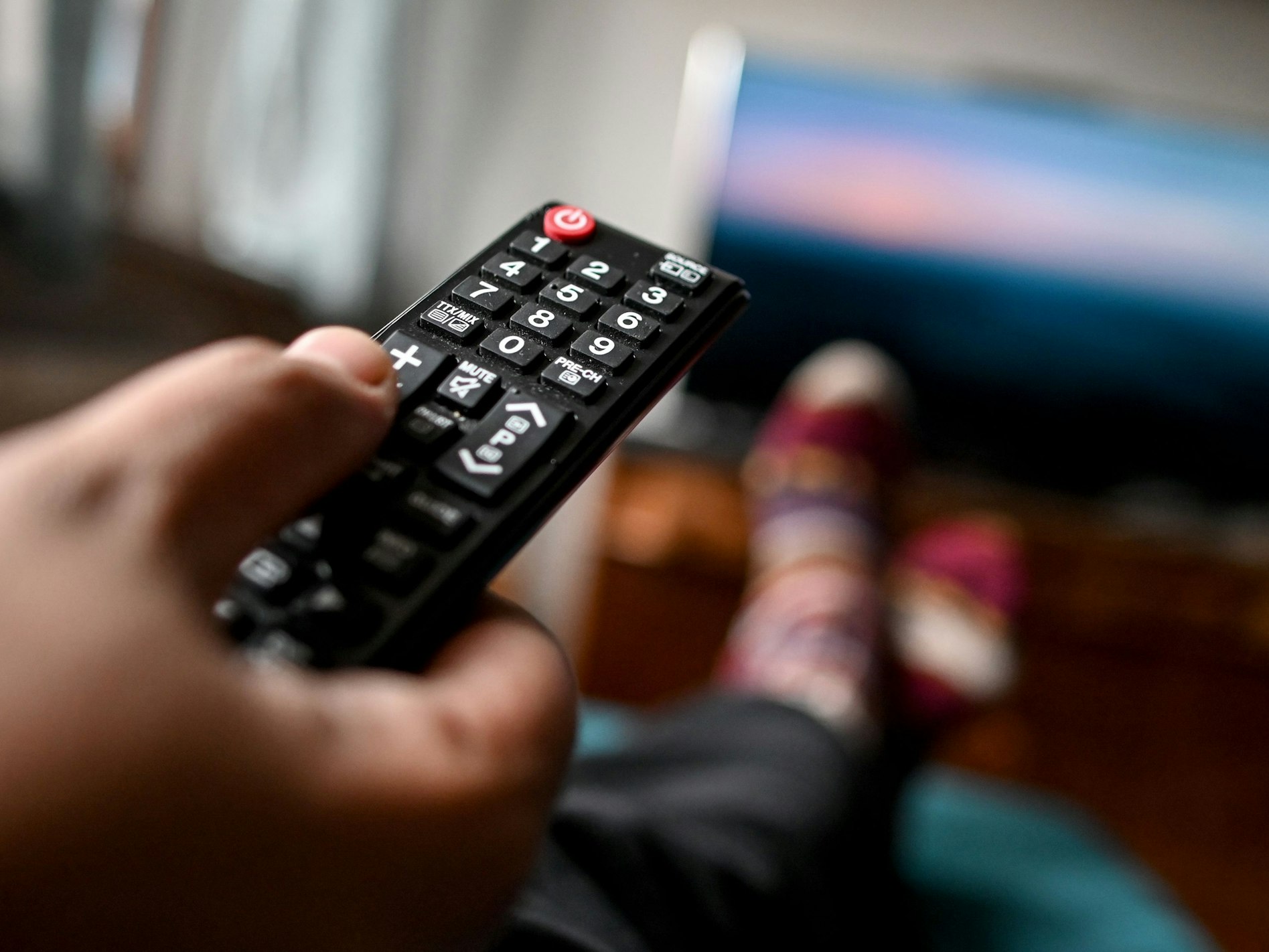Ein junger Mann sitzt mit einer Fernbedienung vor einem Fernseher.