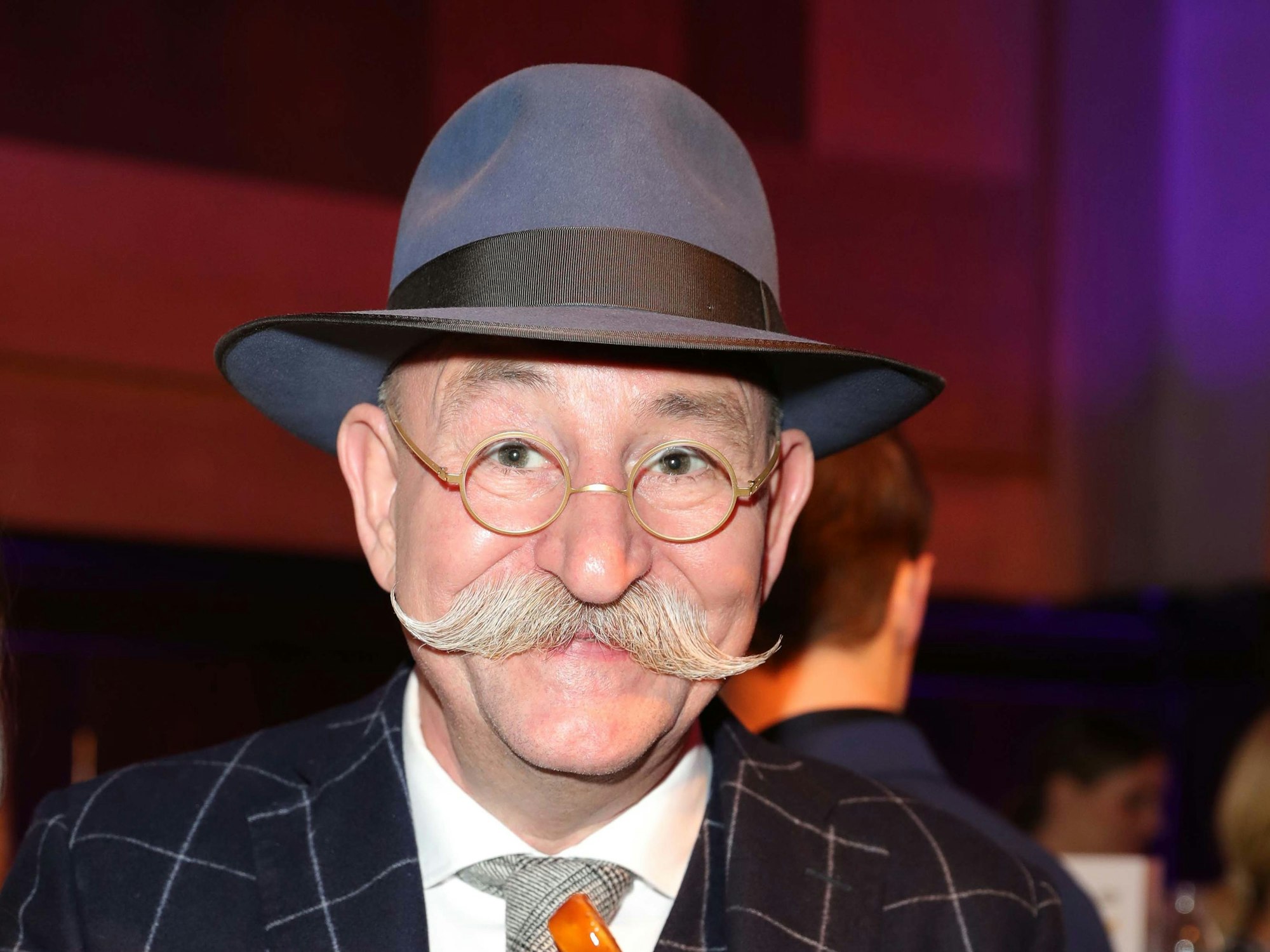Horst Lichter lächelt beim Deutschen Fernsehpreis in einem Anzug in die Kamera und isst Pommes mit Currywurst.