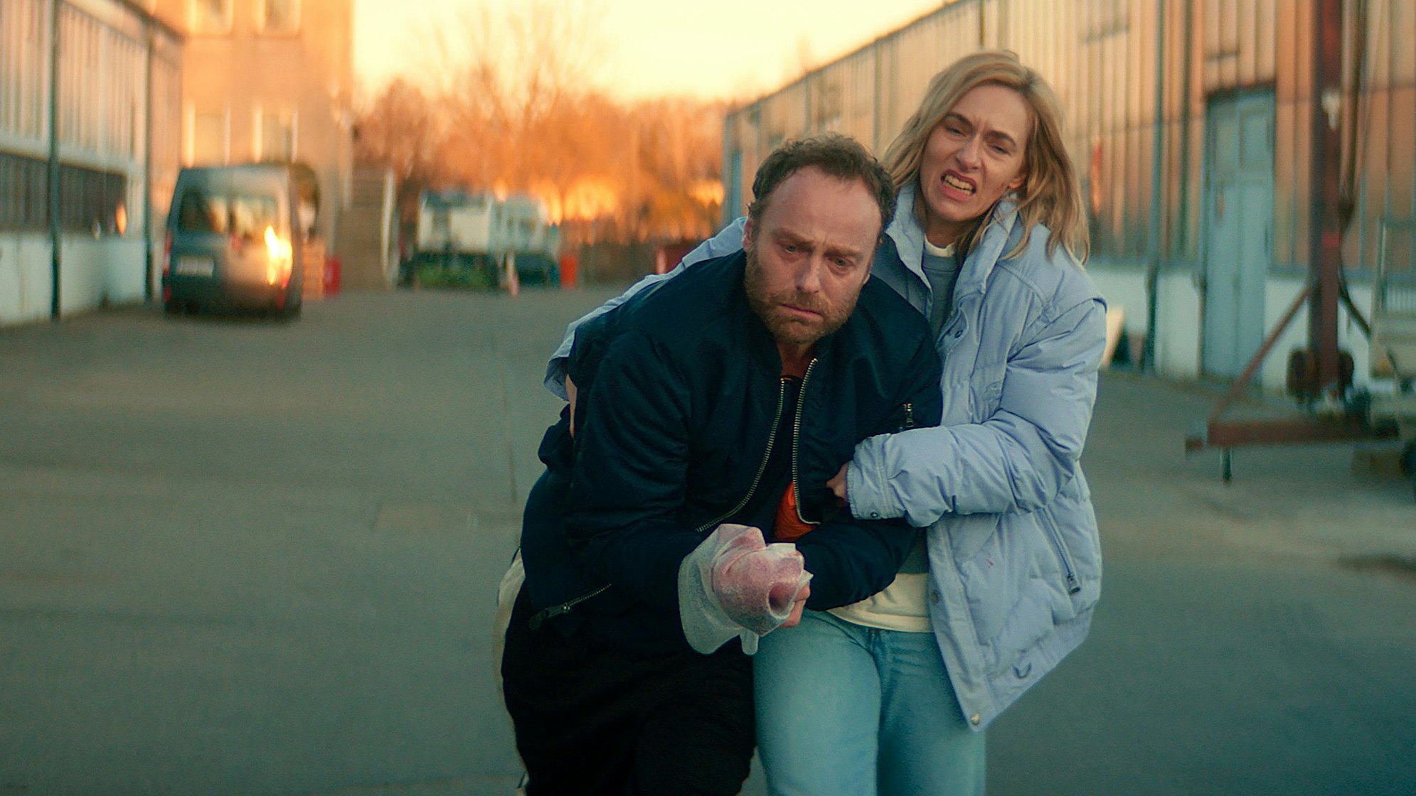 Camilla (Kim Riedle, r.) schleppt den verletzten Robert Karow (Mark Waschke, l.) zum Auto.