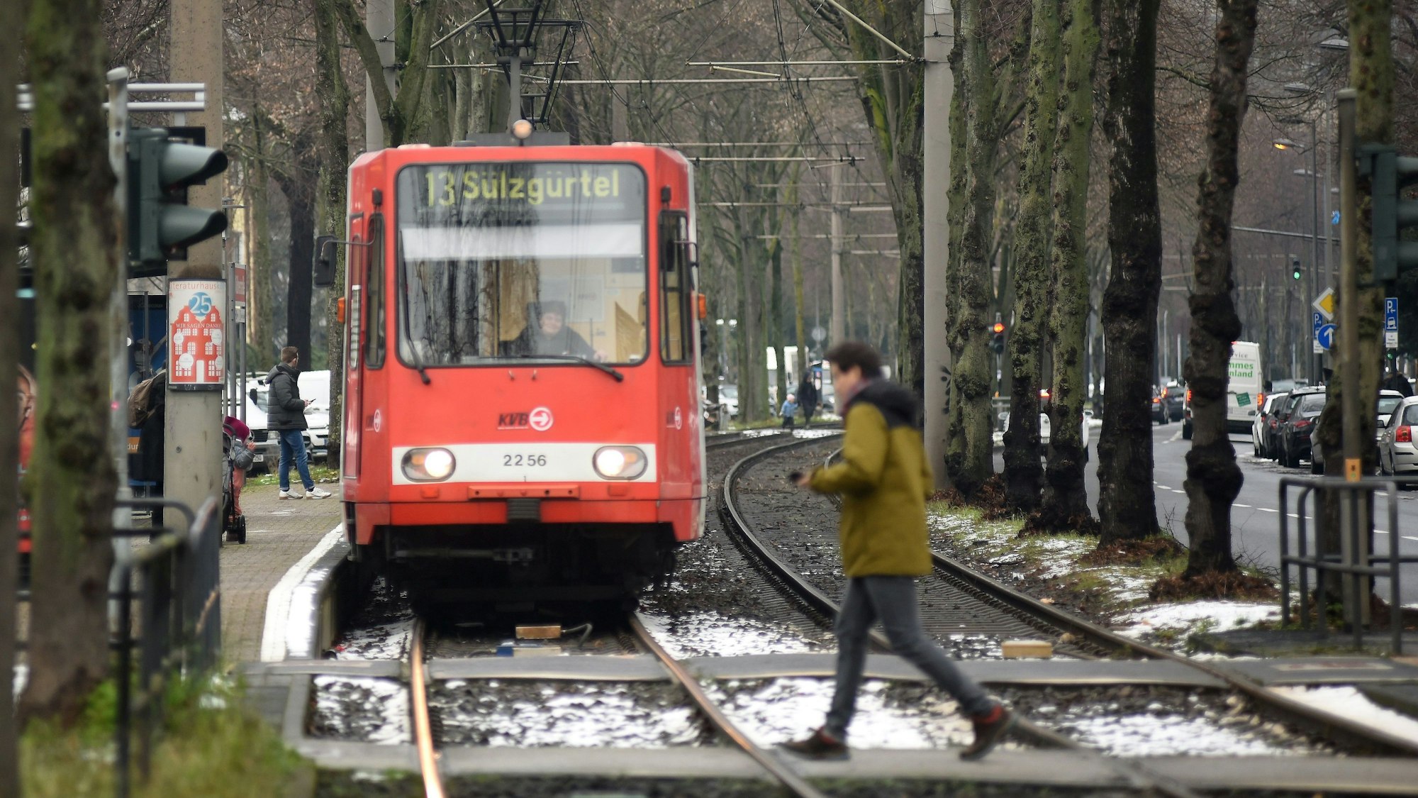 Bahn der KVB-Linie 13 fährt auf die Kamera zu. Im Vordergrund ist ein Mann zu sehen, der die Straße überquert.