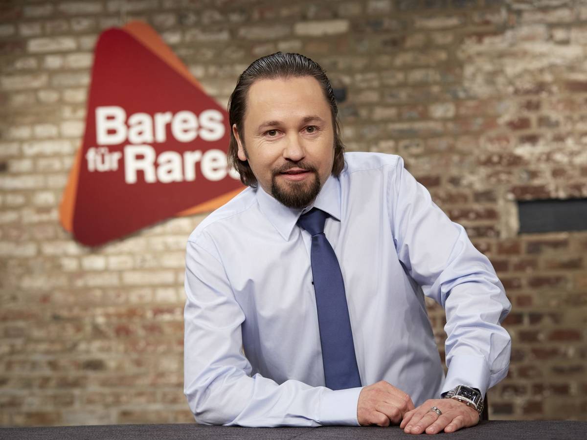 Wolfgang Pauritsch lächelnd vor dem Logo der ZDF-Trödelshow „Bares für Rares“.