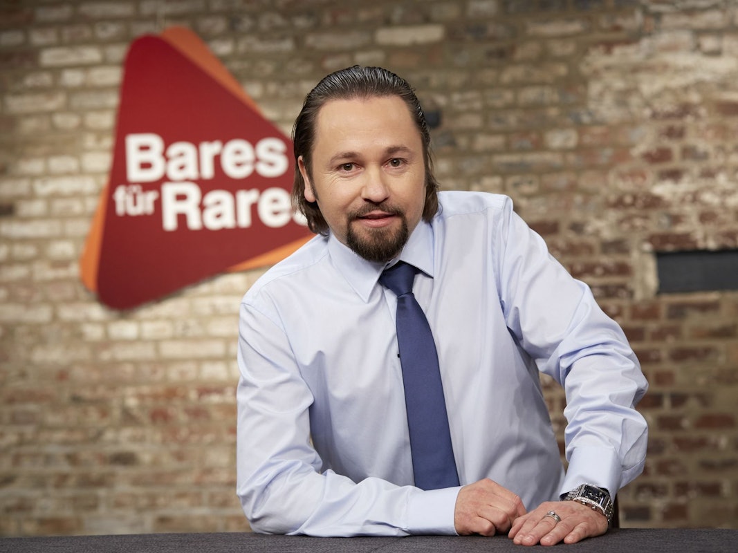 Wolfgang Pauritsch lächelnd vor dem Logo der ZDF-Trödelshow „Bares für Rares“.