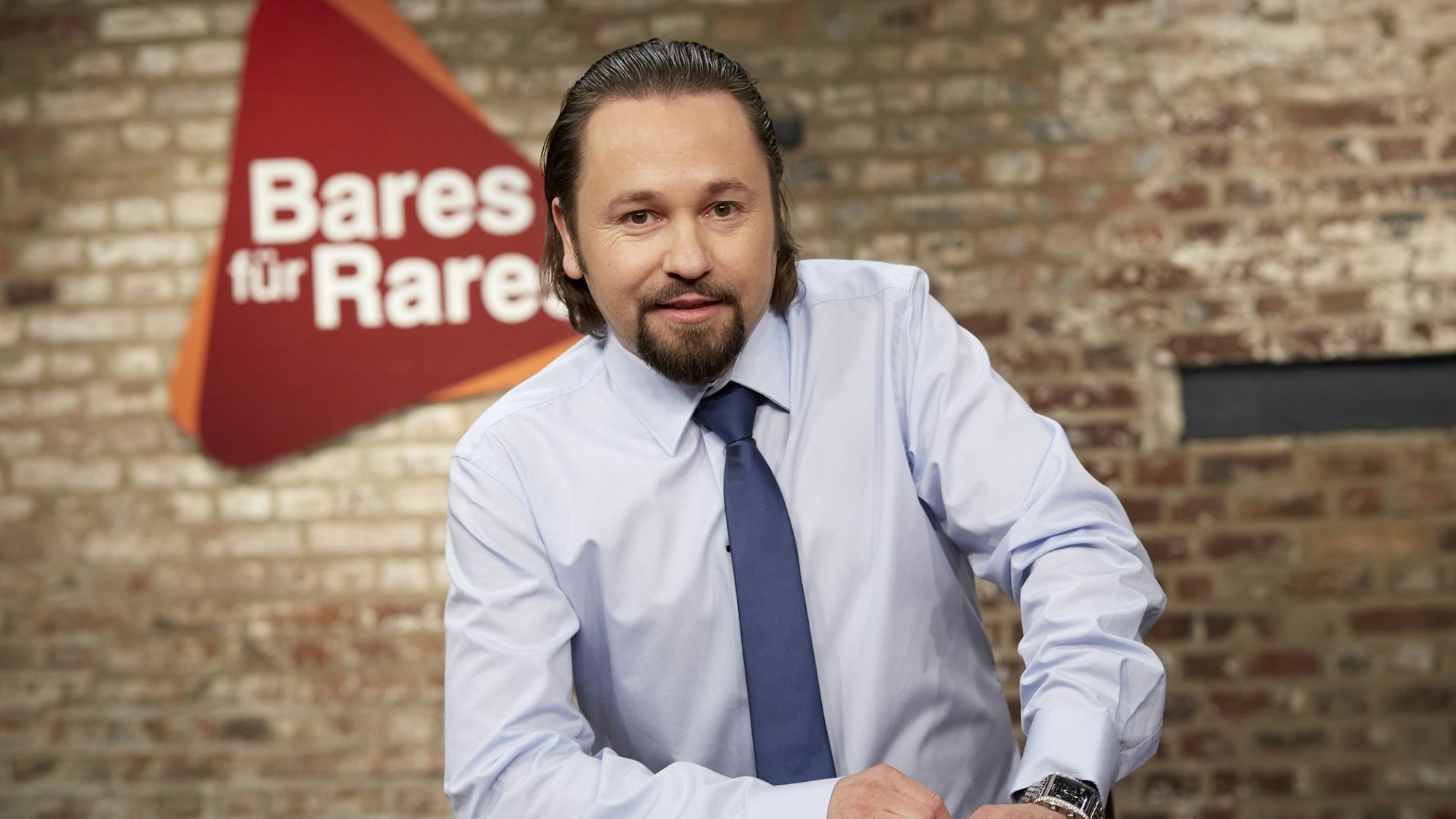 Wolfgang Pauritsch lächelnd vor dem Logo der ZDF-Trödelshow „Bares für Rares“.