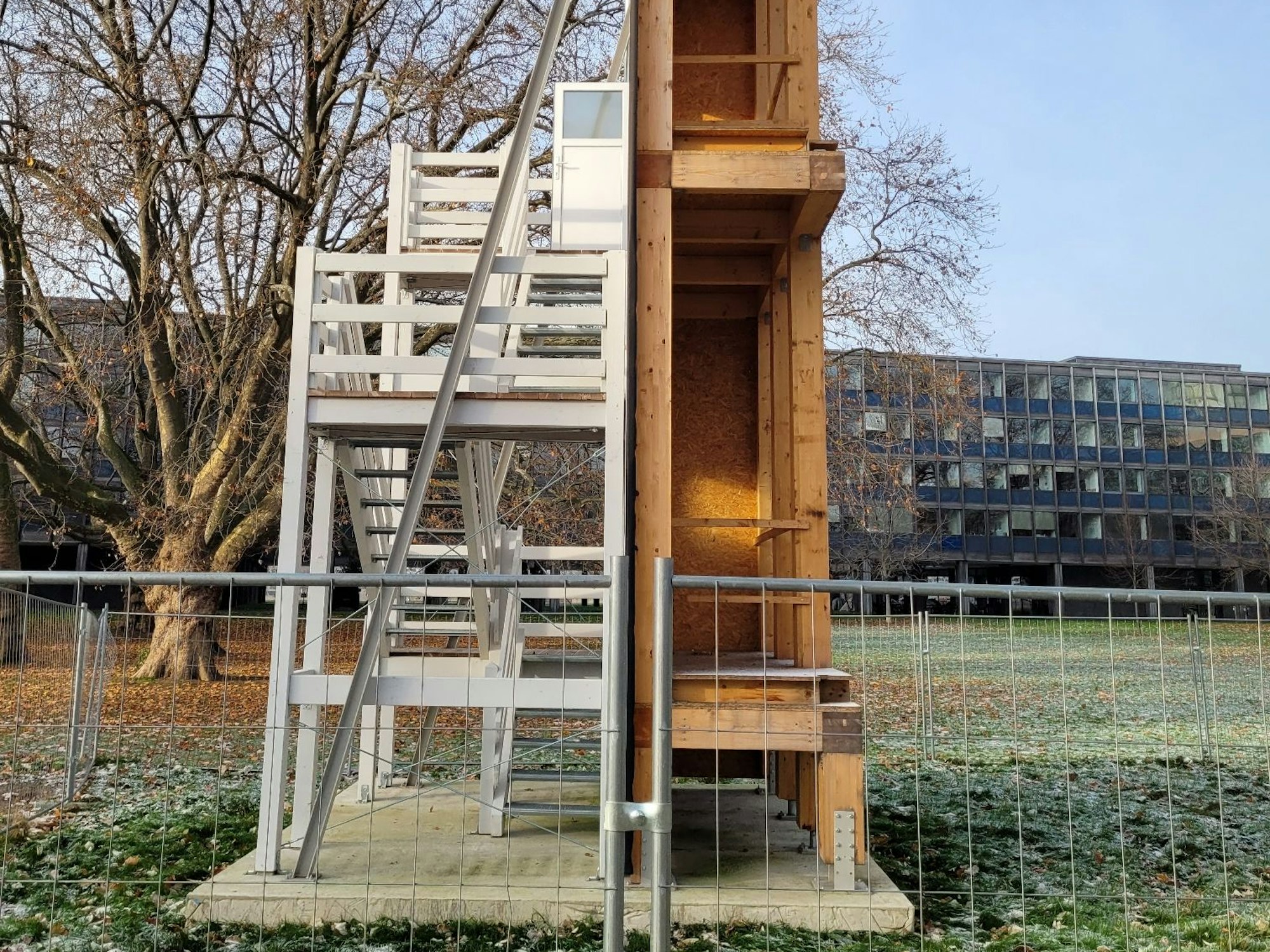 Kleines Bauwerk in Köln von der Seite. Vorne ist eine Holzoptik zu sehen, hinten ist der Bau komplett weiß.