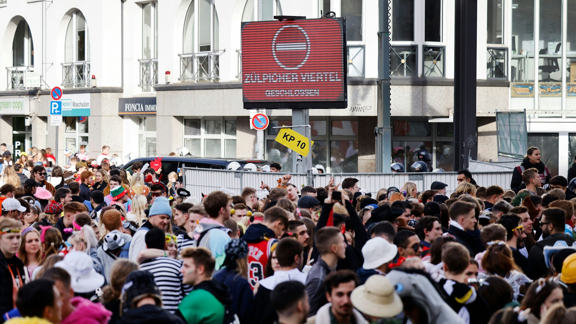 Zahlreiche Karnevalisten stehen an einer Absperrung, da Polizeibeamte den Zugang zur Zülpicher Straße wegen Überfüllung abgeriegelt haben.