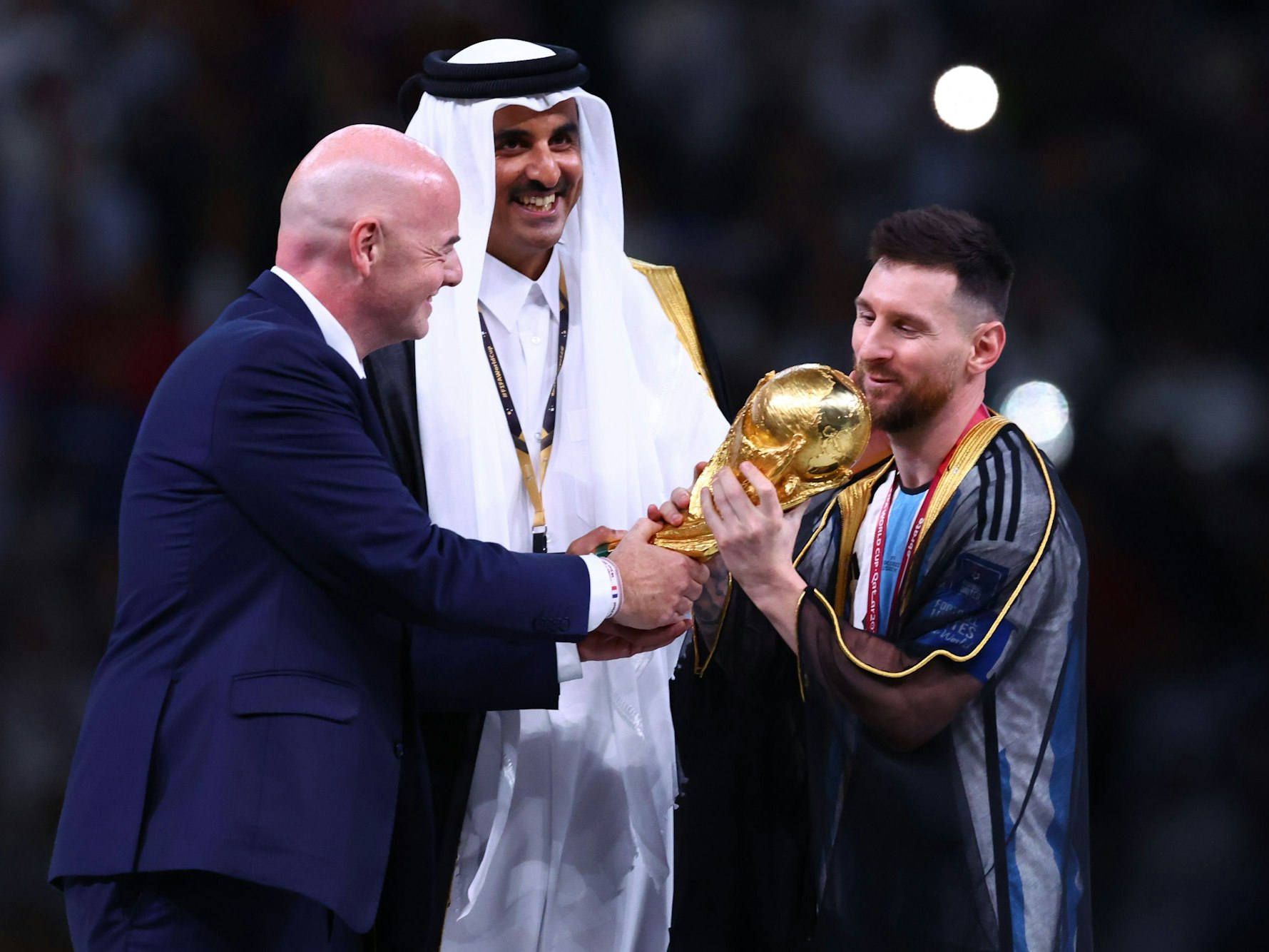 Argentiniens Lionel Messi (r) nimmt den Weltmeisterpokal vom Emir von Katar, Scheich Tamim bin Hamad Al Thani (M) und FIFA-Präsident Gianni Infantino entgegen.