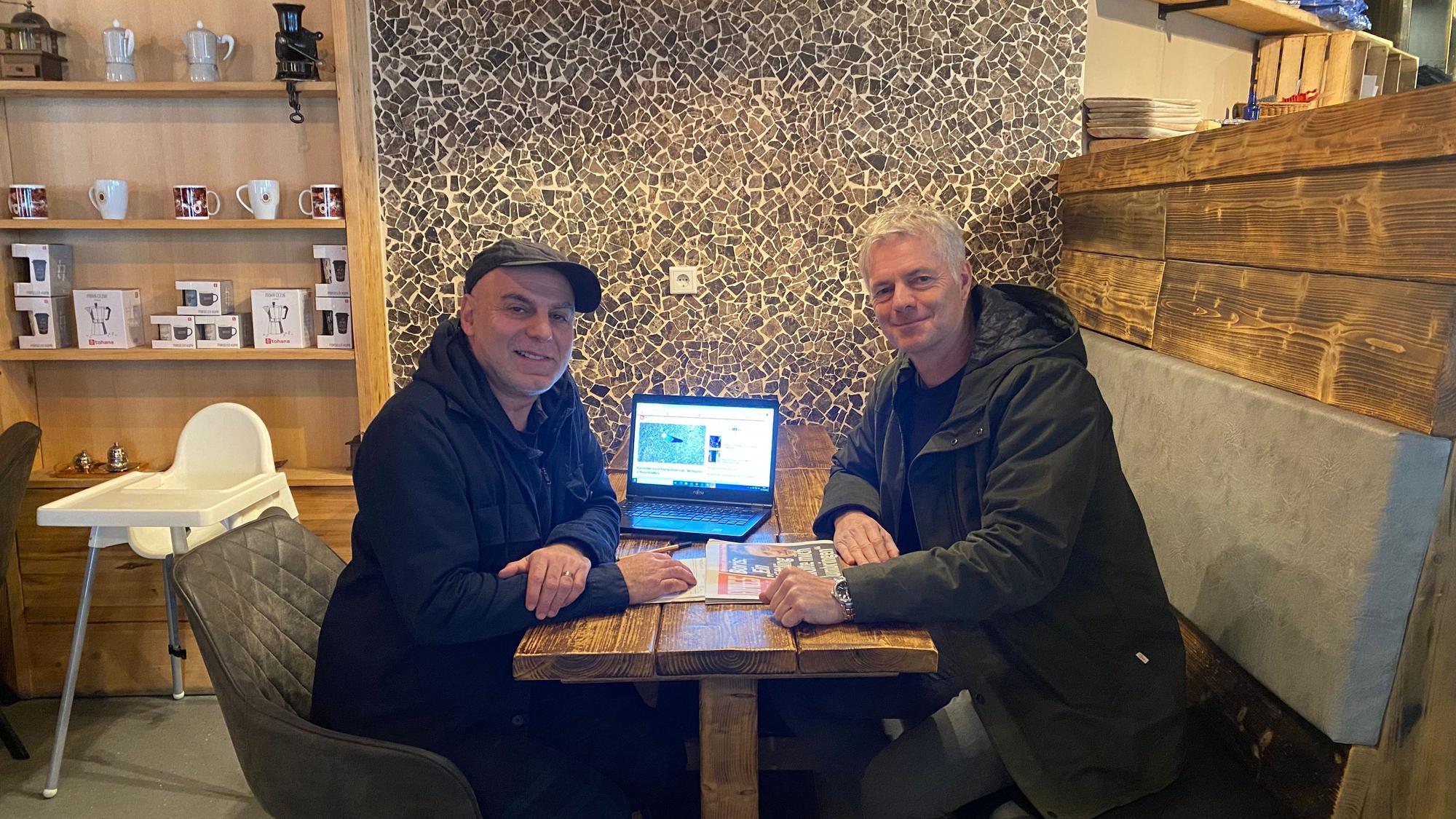 EXPRESS-Reporter Ayhan Demirci sitzt mit ARD-Kommentator Tom Bartels am Tisch.
