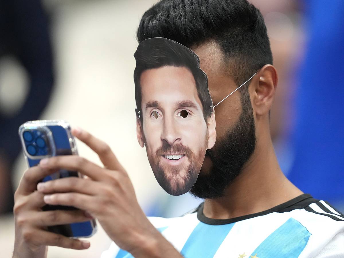 Ein Fan mit der Gesichtsmaske von Argentiniens Lionel Messi bedient sein Smartphone.