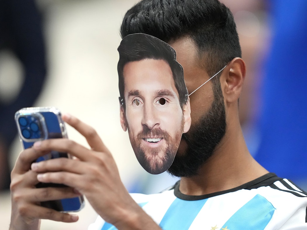 Ein Fan mit der Gesichtsmaske von Argentiniens Lionel Messi bedient sein Smartphone.