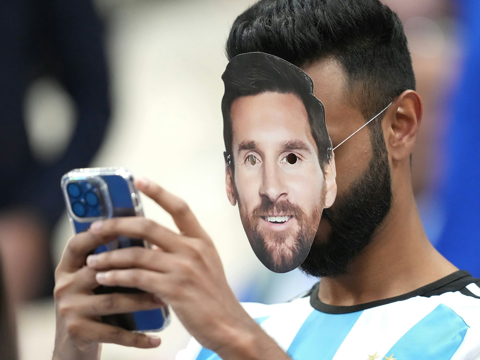 Ein Fan mit der Gesichtsmaske von Argentiniens Lionel Messi bedient sein Smartphone.